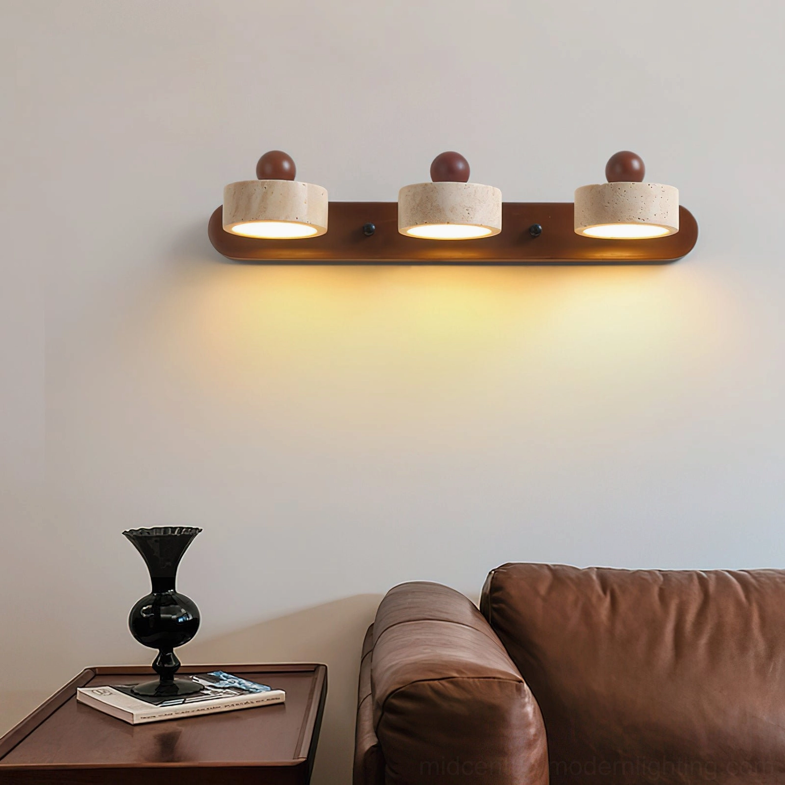 Piero 3-light travertine wall sconce in living room above leather sofa, mid-century modern decor