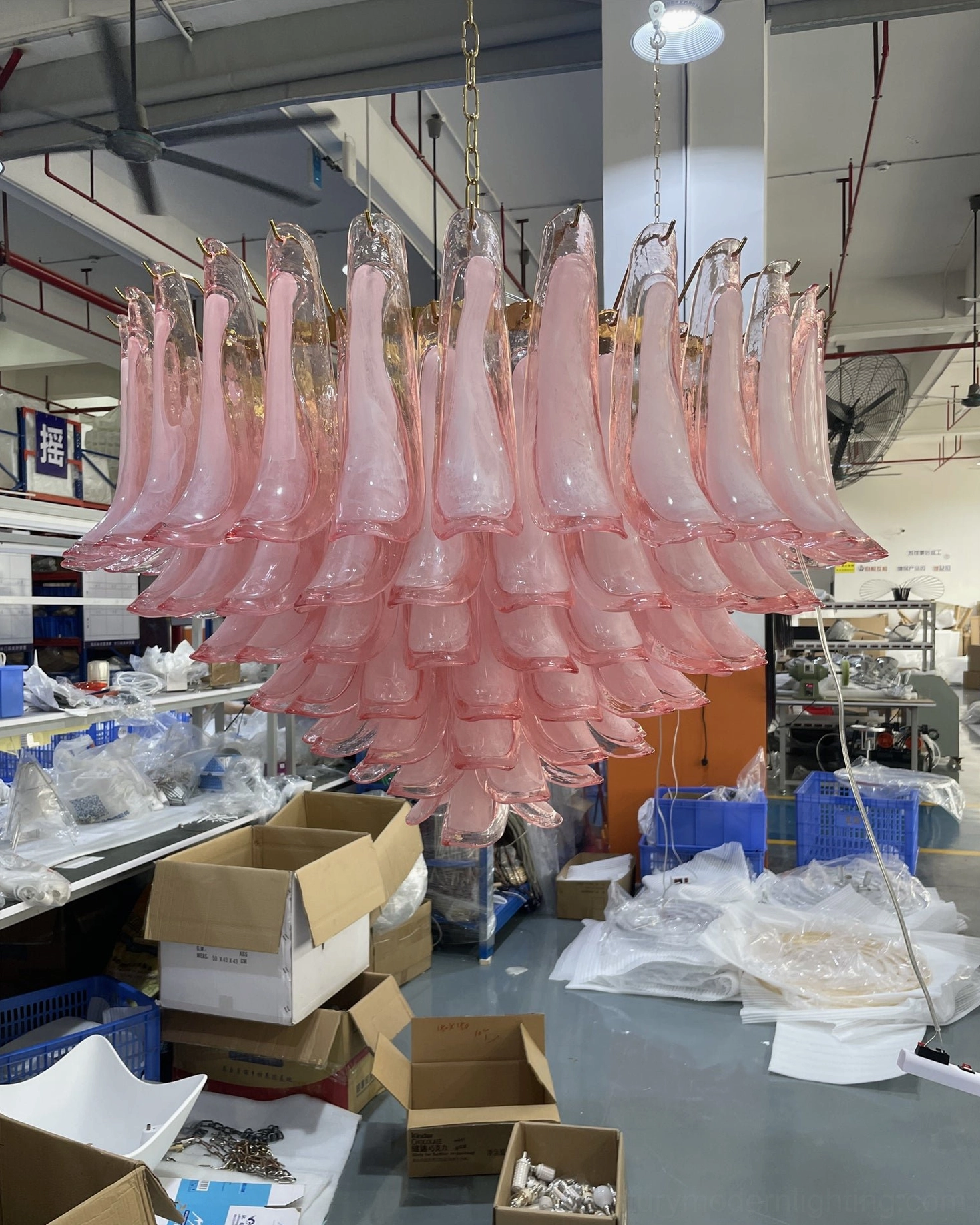 Pink Murano glass chandelier in warehouse production facility surrounded by packaging and manufacturing supplies