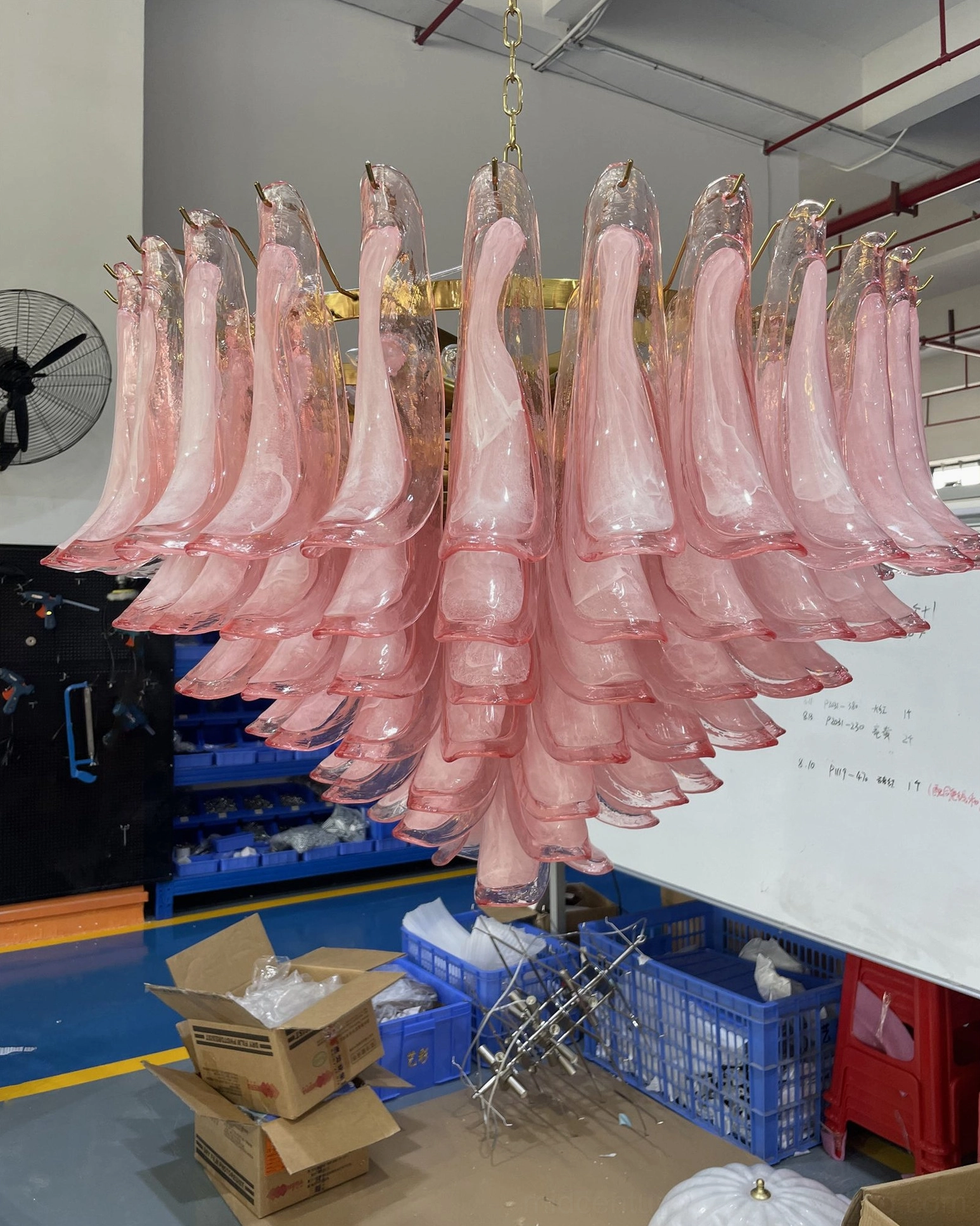Unassembled pink Murano glass chandelier components in factory showing individual hand-blown glass petals and gold metal hardware