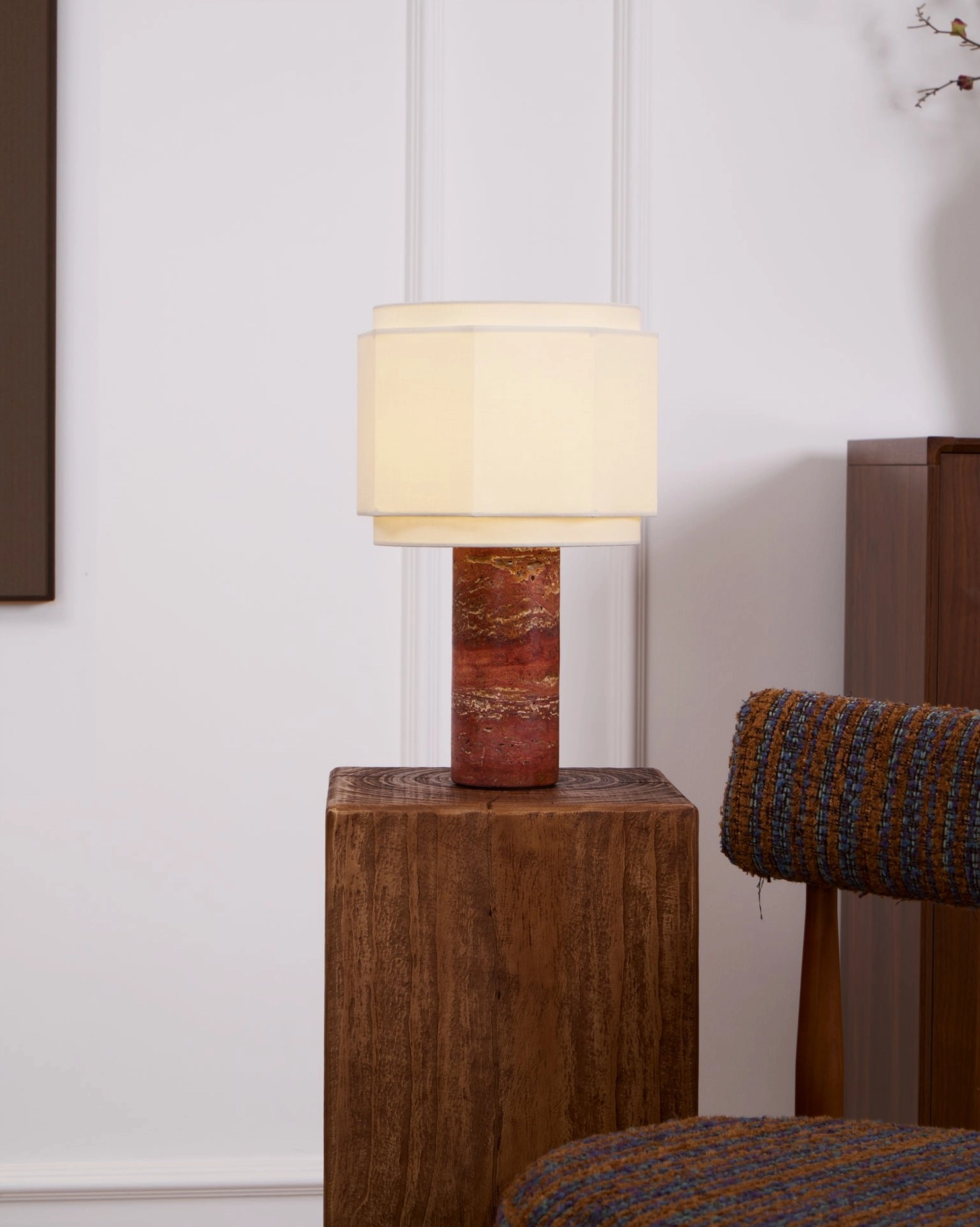 Pipito red travertine lamp positioned in minimalist home corner with wood pedestal and woven seating