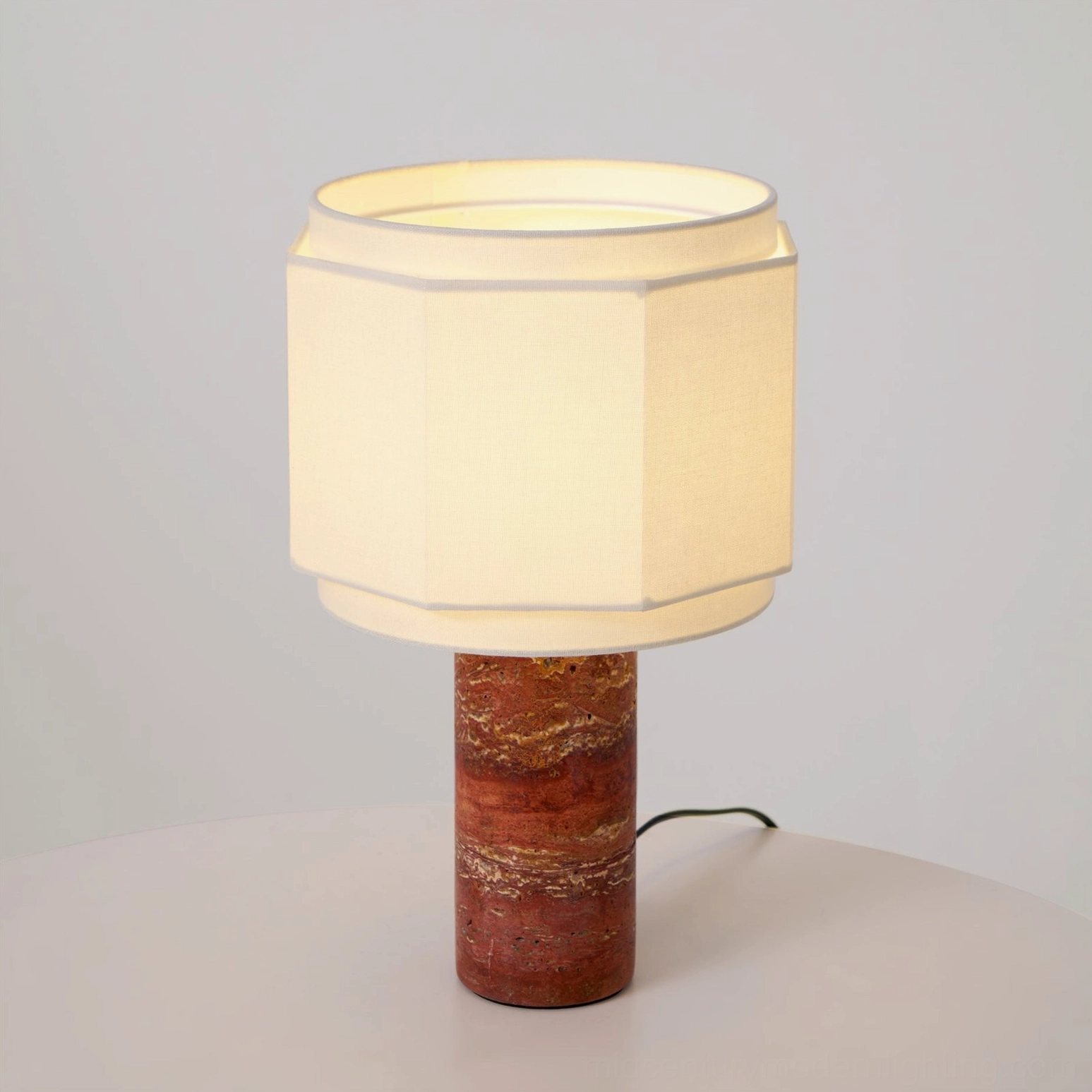 Close-up detail of Pipito lamp showing travertine stone base and power cord on round side table