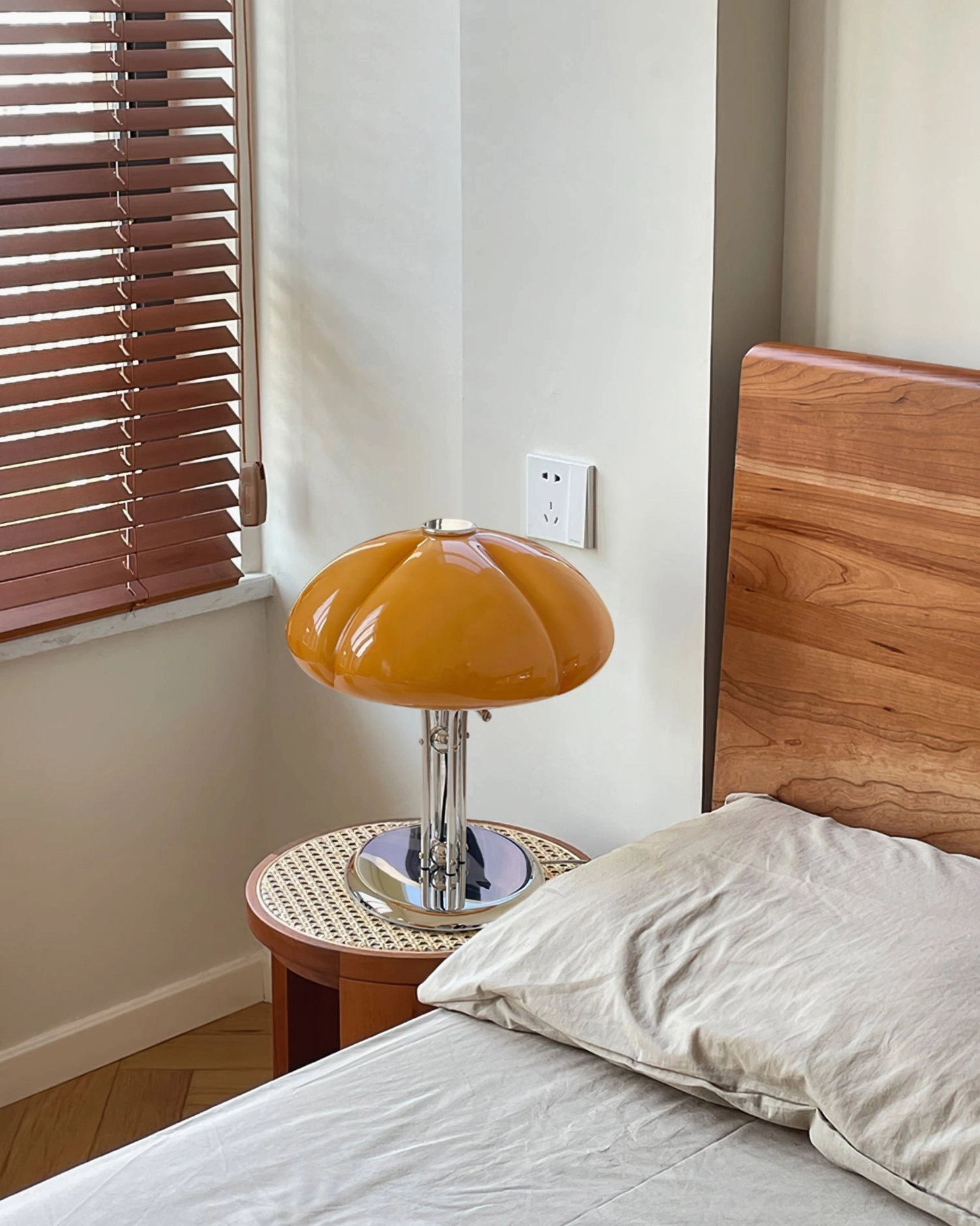Quadrifoglio table lamp on bedroom bedside surface near window blinds, warm amber glow and chrome stand