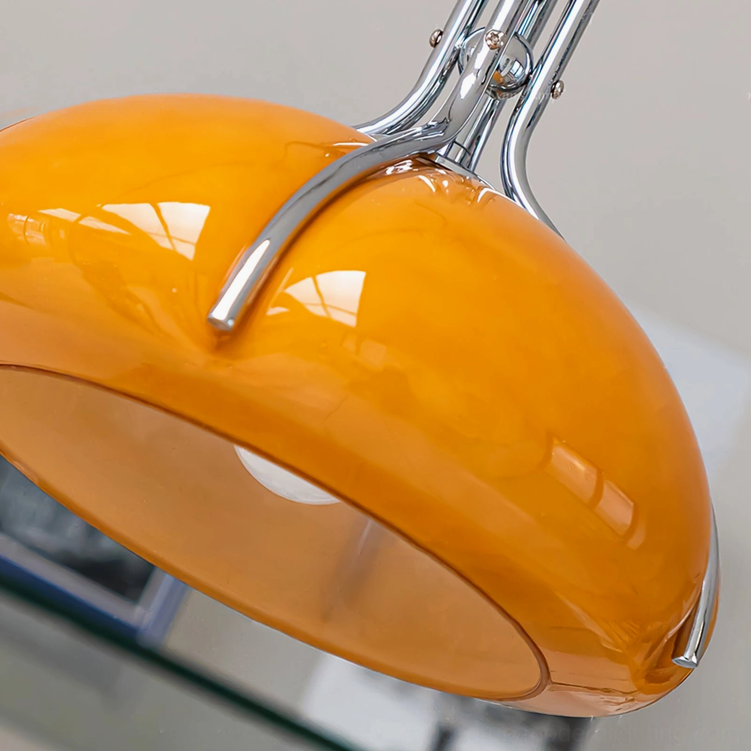 Close-up of Quadrifoglio pendant lamp shade showing glossy amber glass and chrome trim