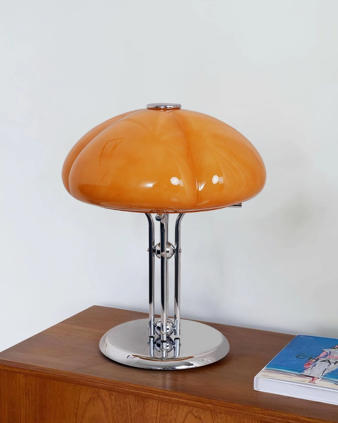 Quadrifoglio pumpkin-style table lamp on wooden dresser top, side view showing light amber glossy finish and sleek chrome base