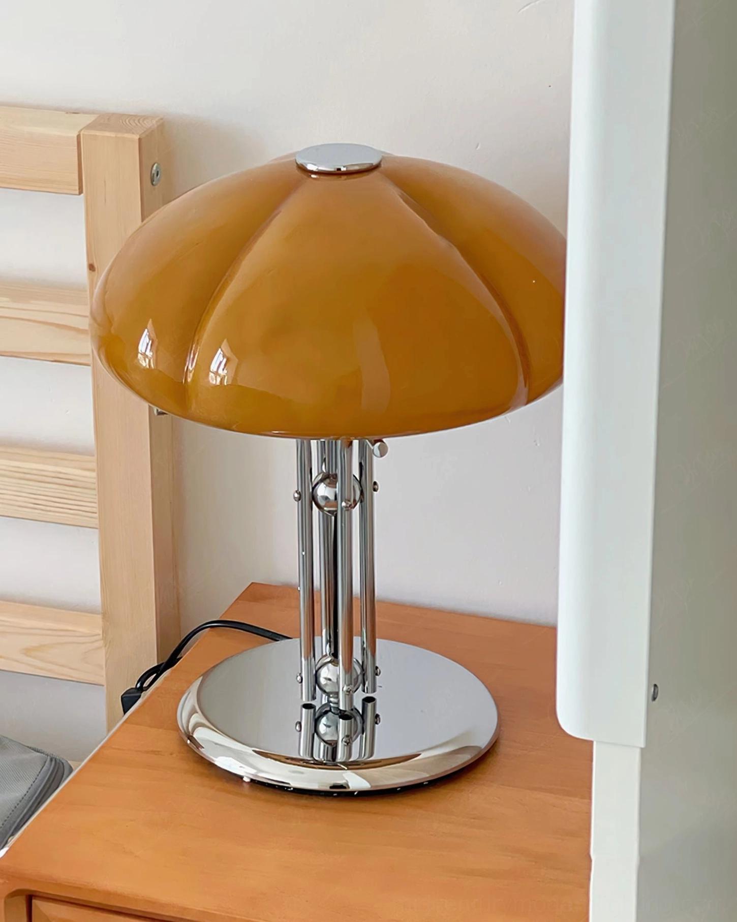 Quadrifoglio table lamp on wooden bedside table, front three-quarter angle, deep amber glass shade with adjustable chrome stem