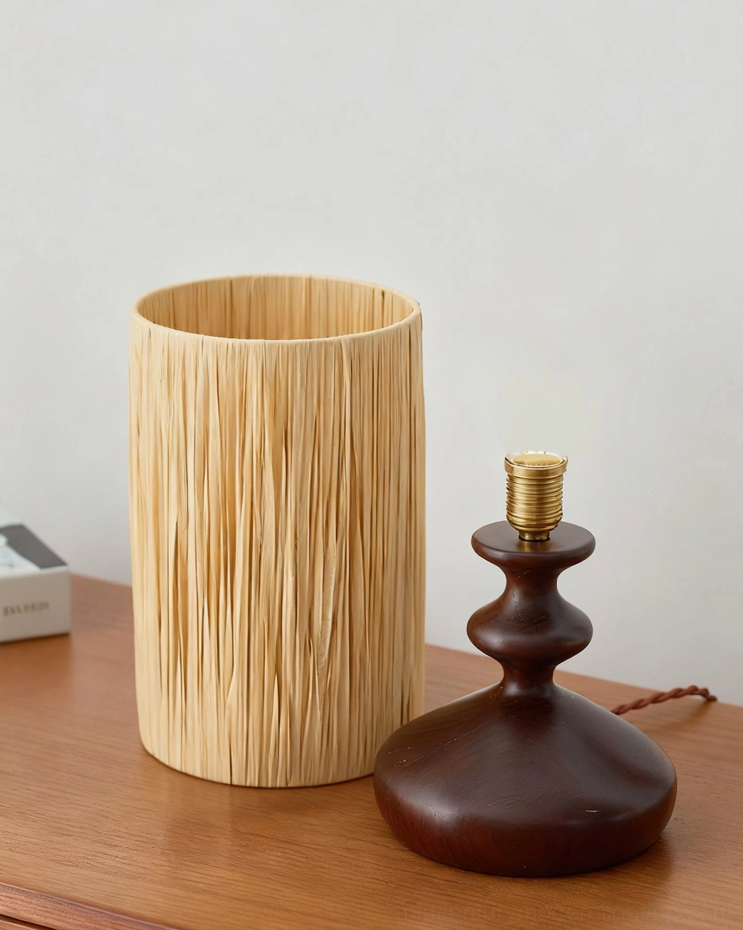 Disassembled raffia table lamp components showing shade and wooden base with brass socket, assembly view