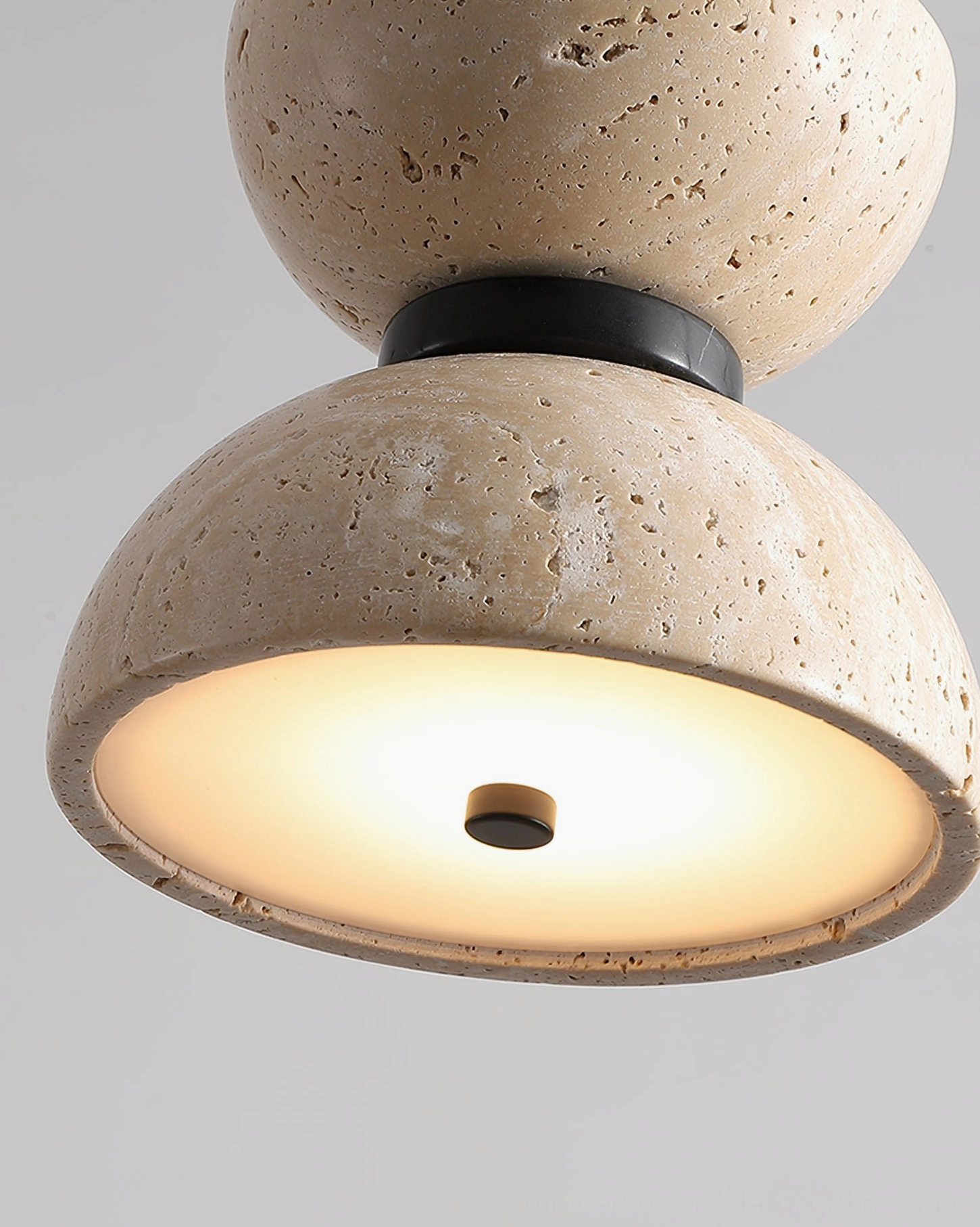 Randolf travertine pendant lamp illuminated with warm glow showing light diffusion through natural stone with black metal accents