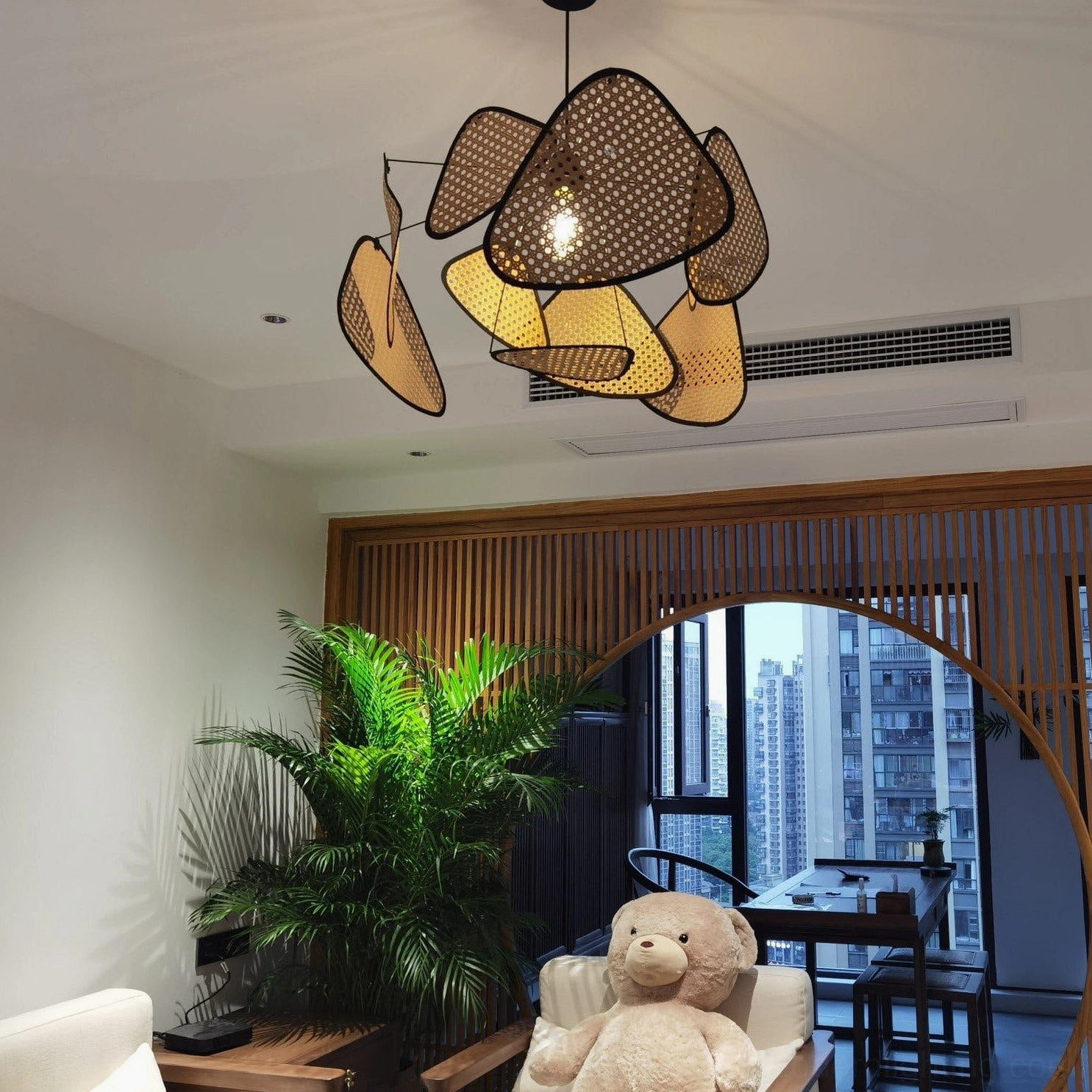 Asymmetrical rattan chandelier in contemporary dining-living space, natural tan-brown woven bamboo shades creating soft lighting