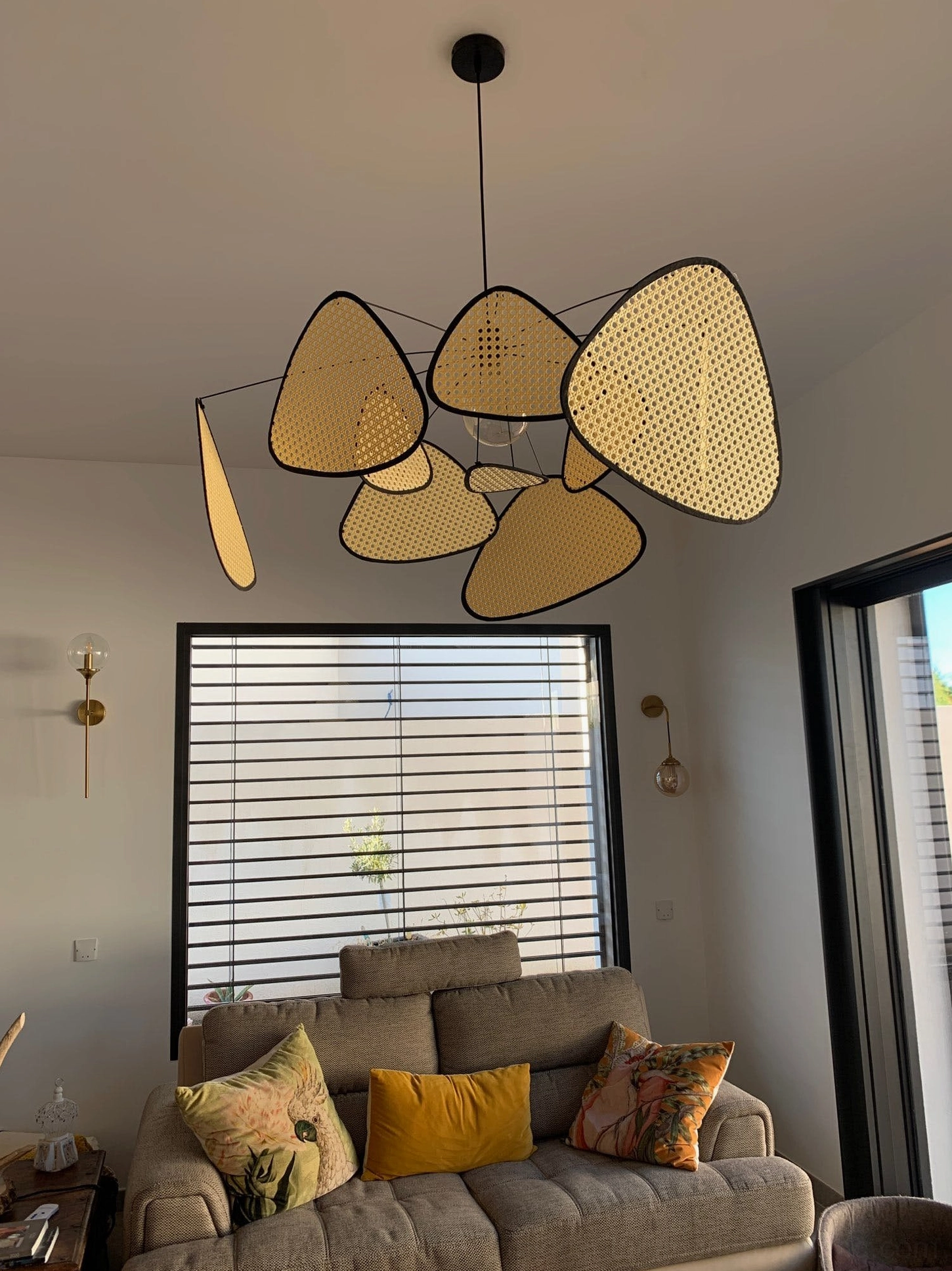 Rattan cluster pendant light above cozy sofa lounge area, soft glowing warm lighting, roller blind window backdrop