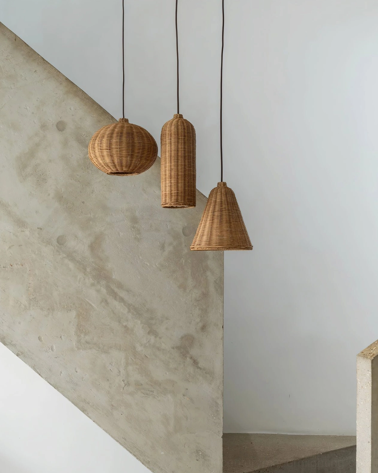 Hand-woven rattan pendant light set viewed from low angle in staircase corner with textured wall, wabi-sabi rustic home style