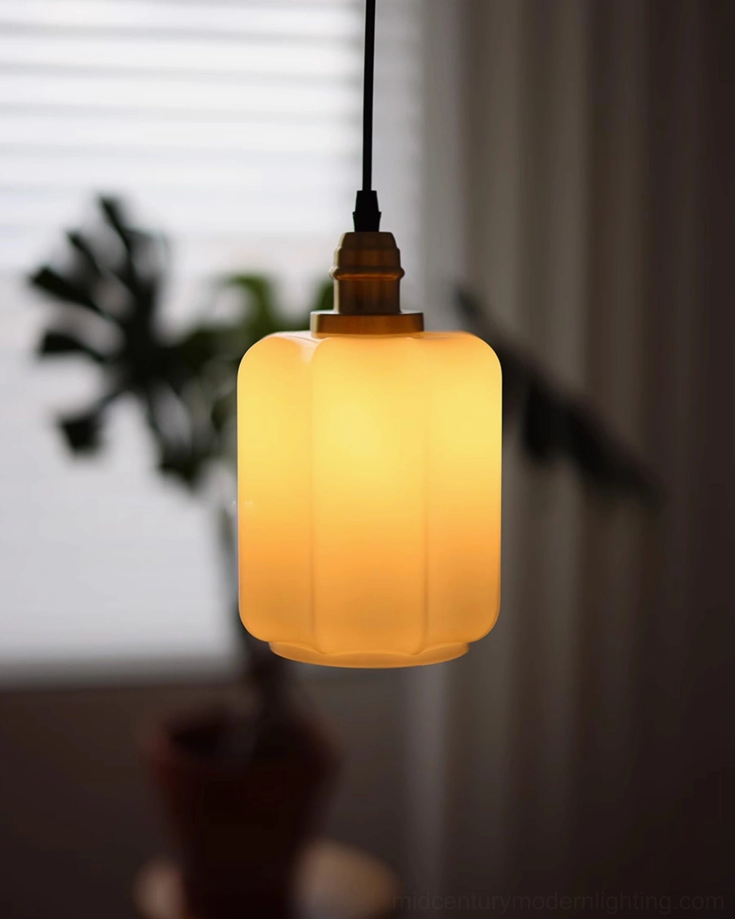 Illuminated Rayburn cylindrical ribbed glass pendant with warm amber glow and brass hardware