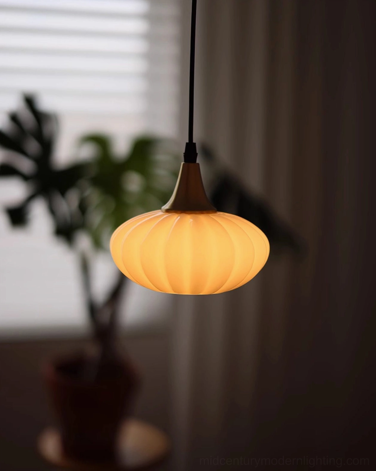 Rayburn pumpkin ribbed pendant light with warm glow in home corner with potted plant and minimalist decor