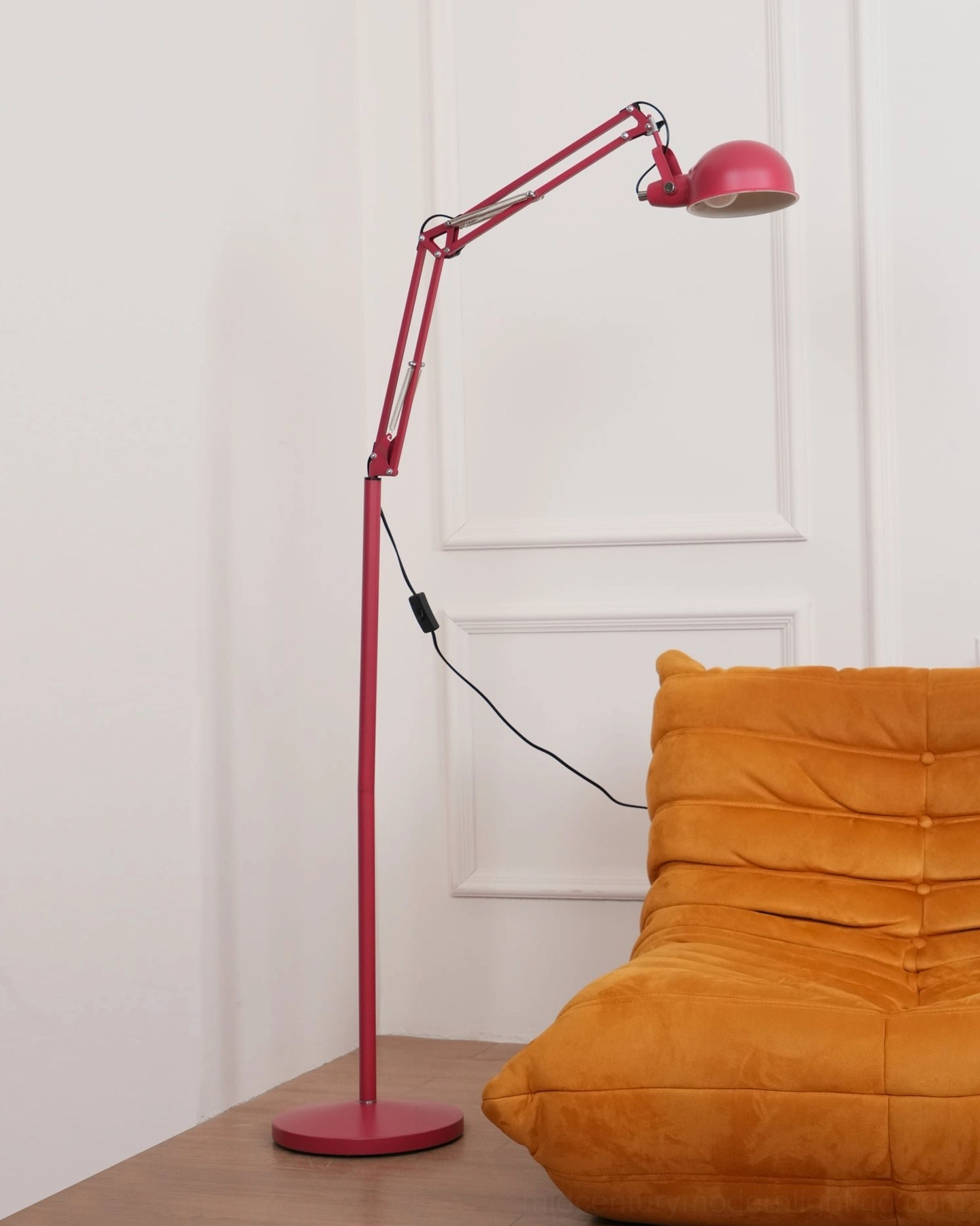 Red swing arm floor lamp in contemporary home setting with orange seating furniture, side view of fully articulated design