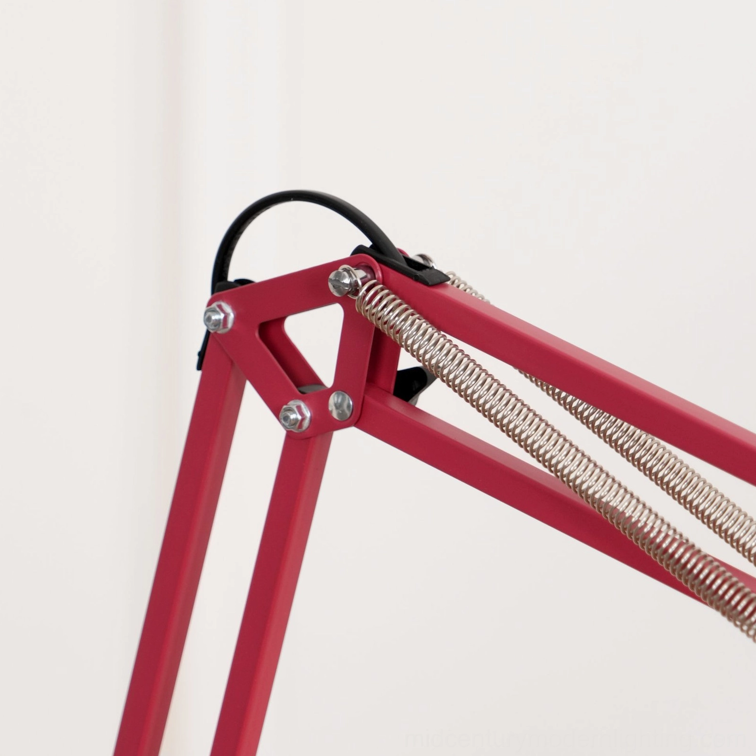 Close-up detail of red floor lamp swing arm joint mechanism showing silver tension spring and precision metal fasteners