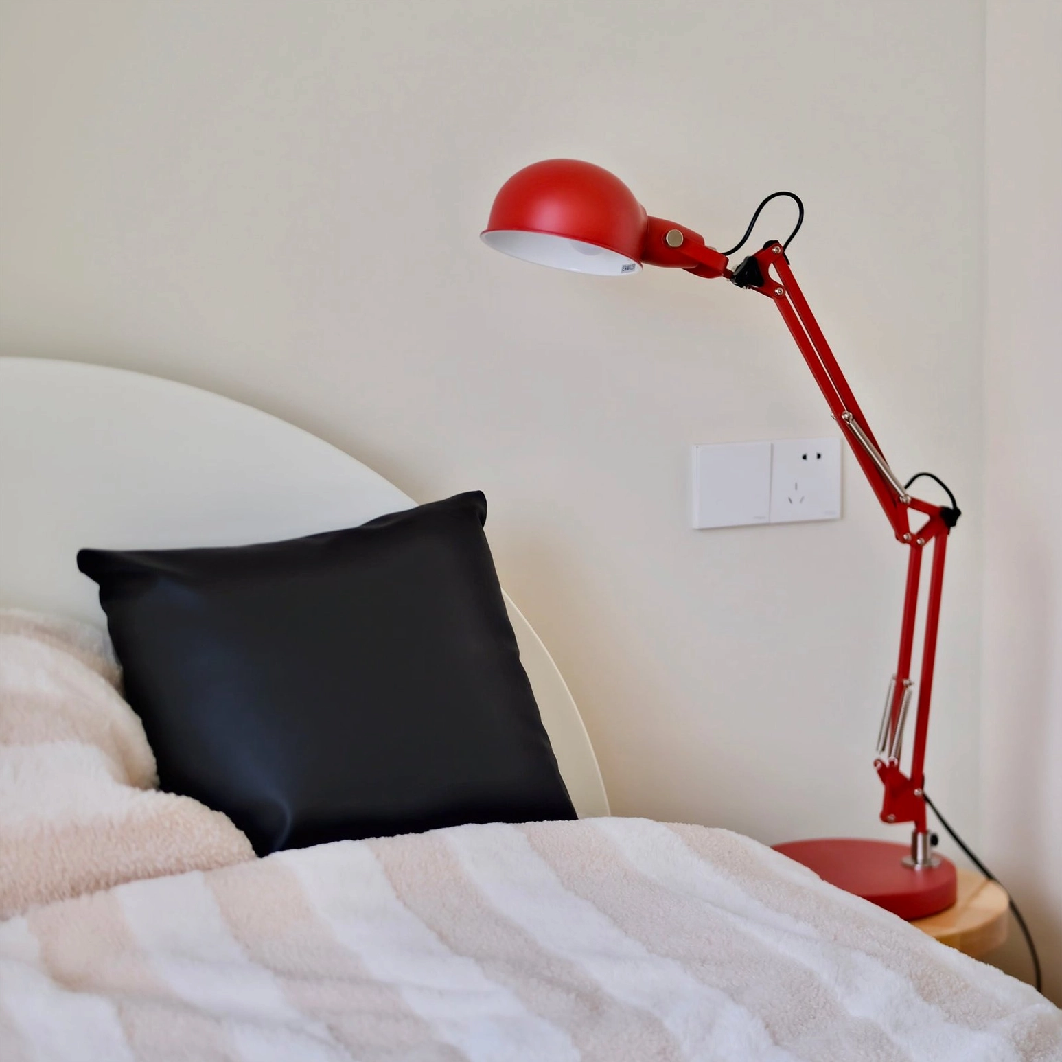 Red desk lamp positioned on bedroom bedside corner next to striped bedding and black throw pillow