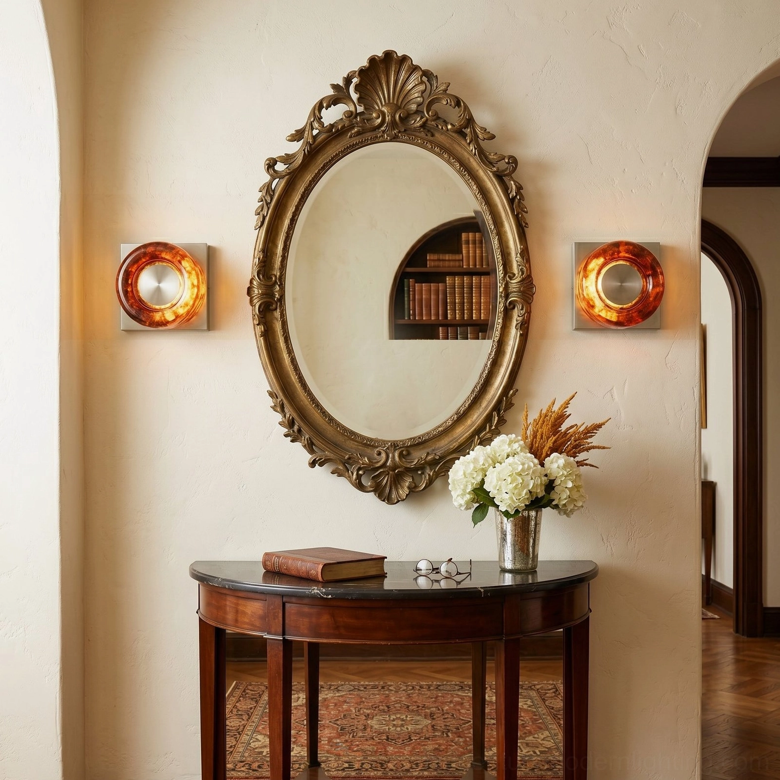 Pair of red wall sconces flanking ornate gilded oval mirror in classic French entryway with console table
