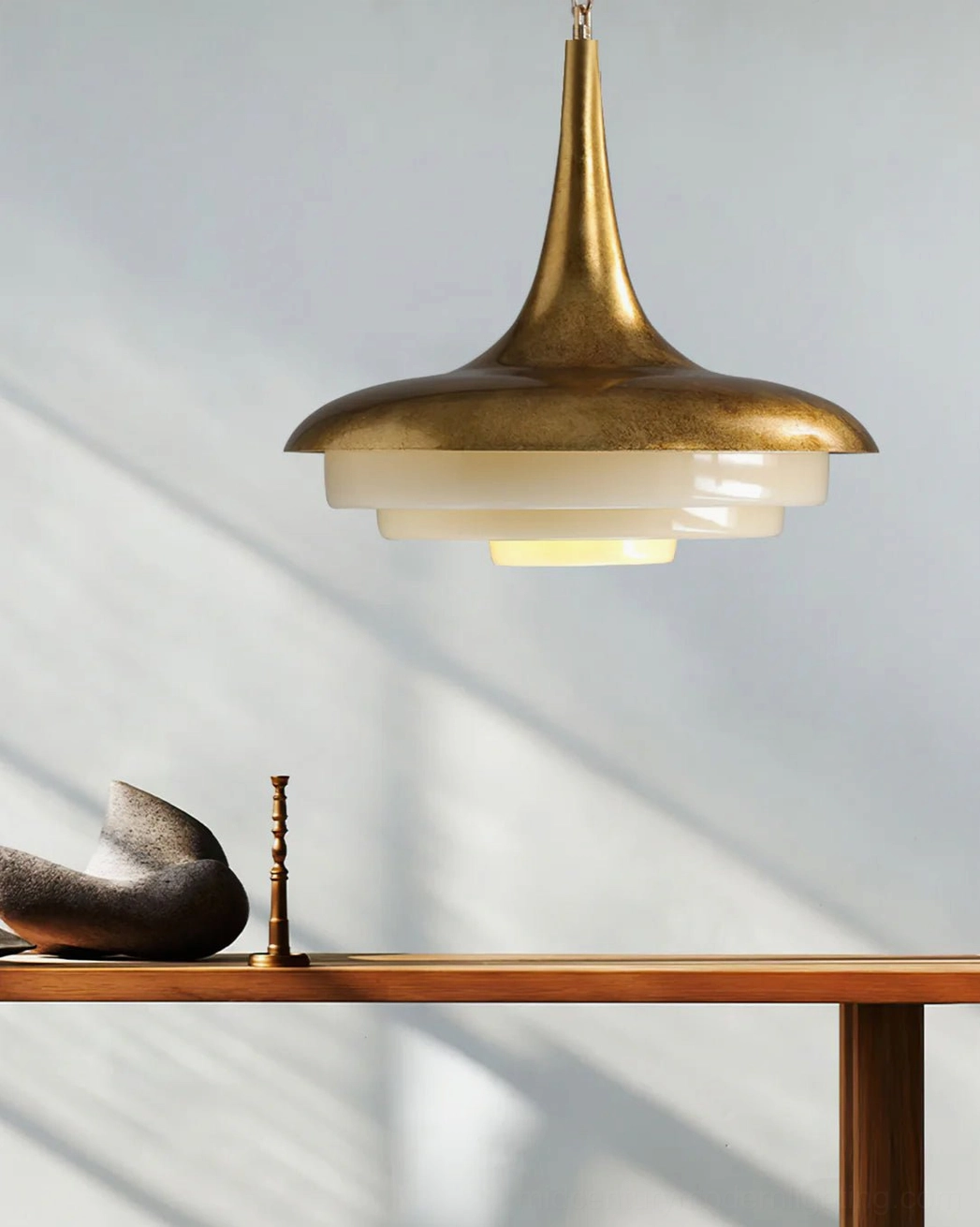 Low angle view of brass tiered pendant lamp with soft shadow casting on white wall