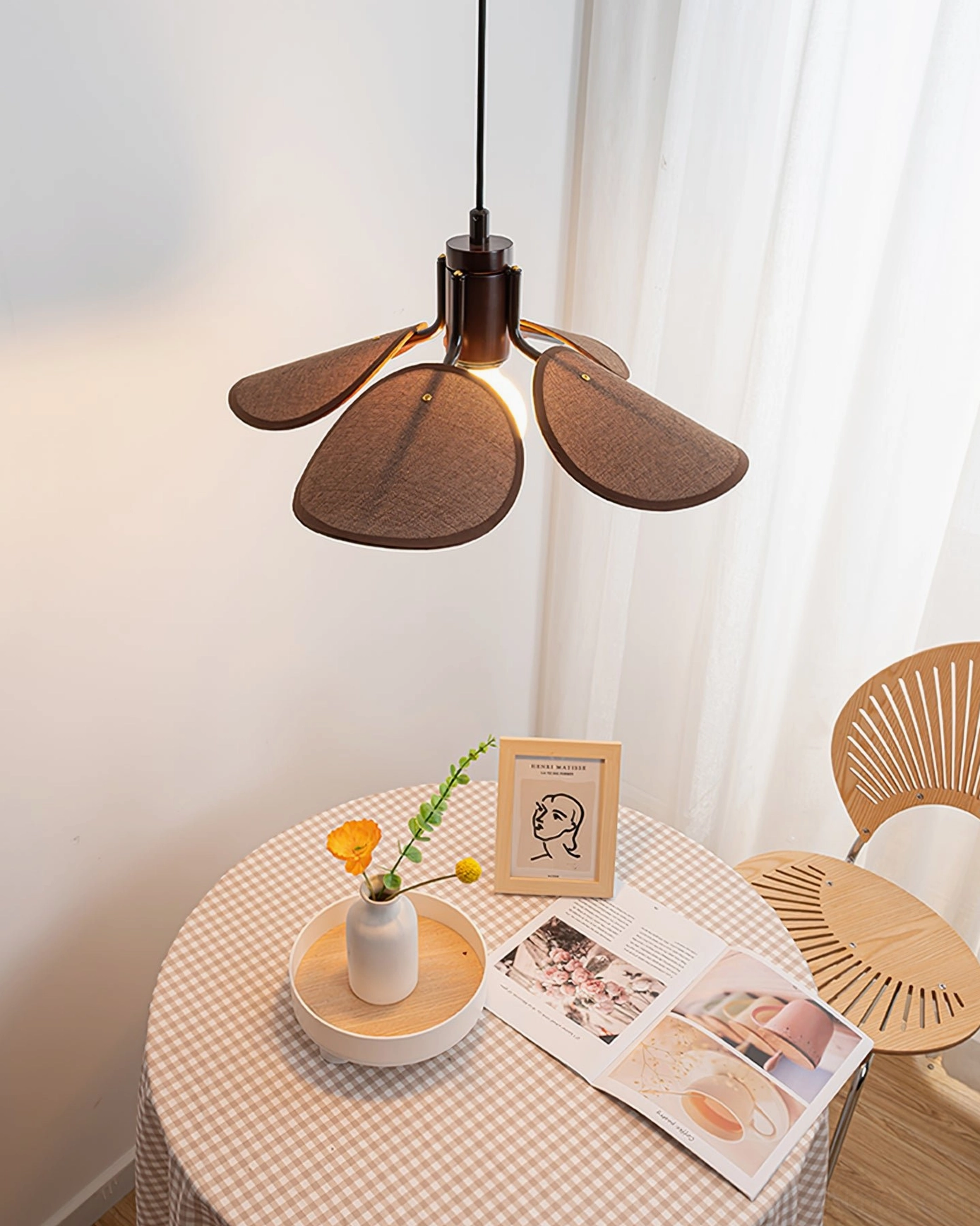 Riankh pendant lamp with dark brown woven petal shade and dark metal fixture hanging above wooden chair in dining nook