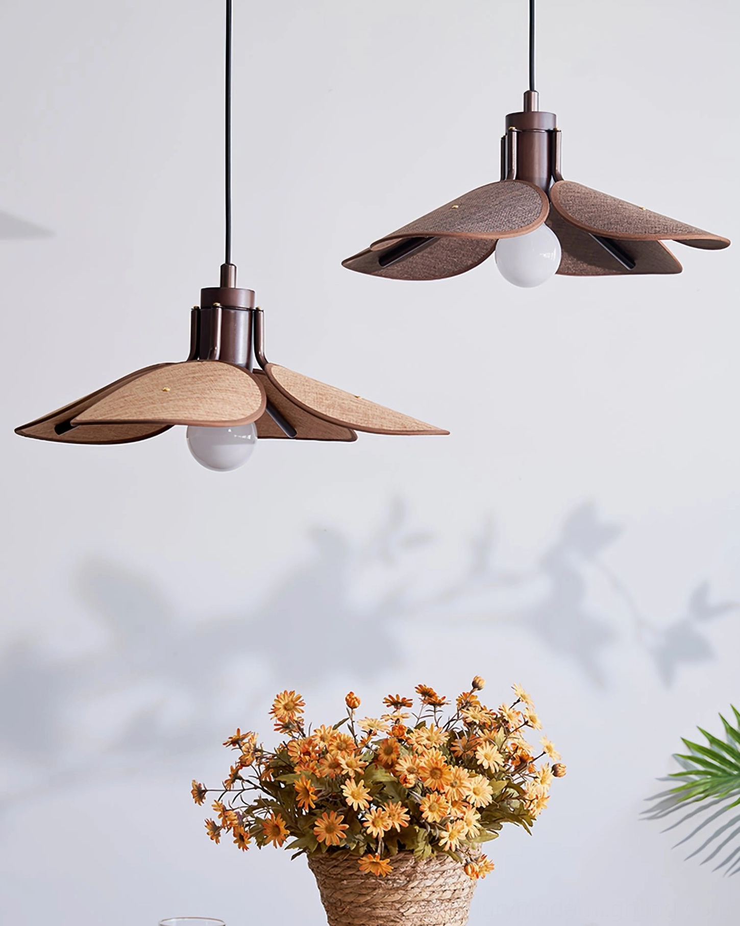 Two Riankh pendant lamps with dark metal hardware and exposed white bulbs, side view against wall with leaf shadow decoration