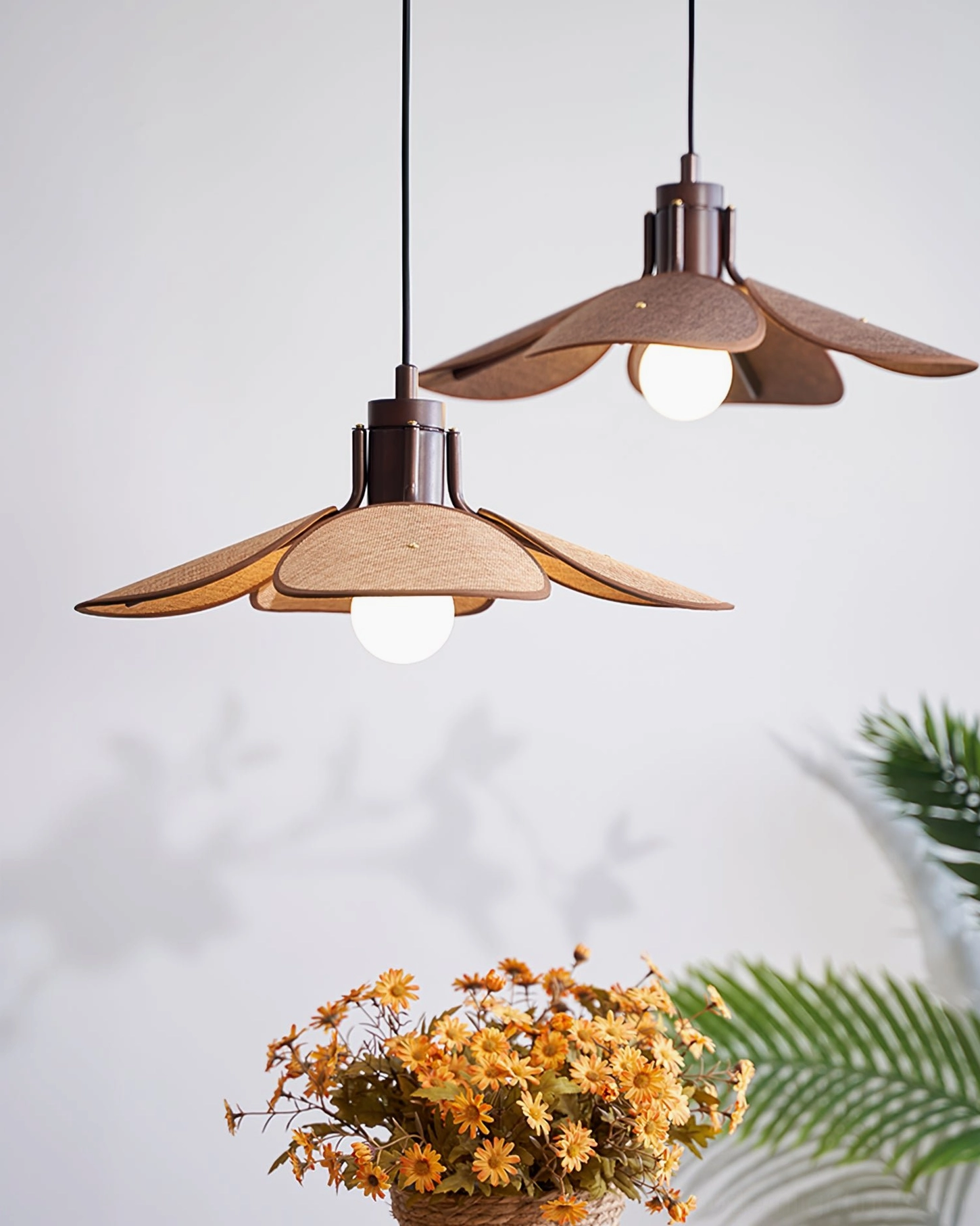 Riankh woven pendant lights with natural texture and illuminated warm glow, front hanging view with green foliage studio backdrop