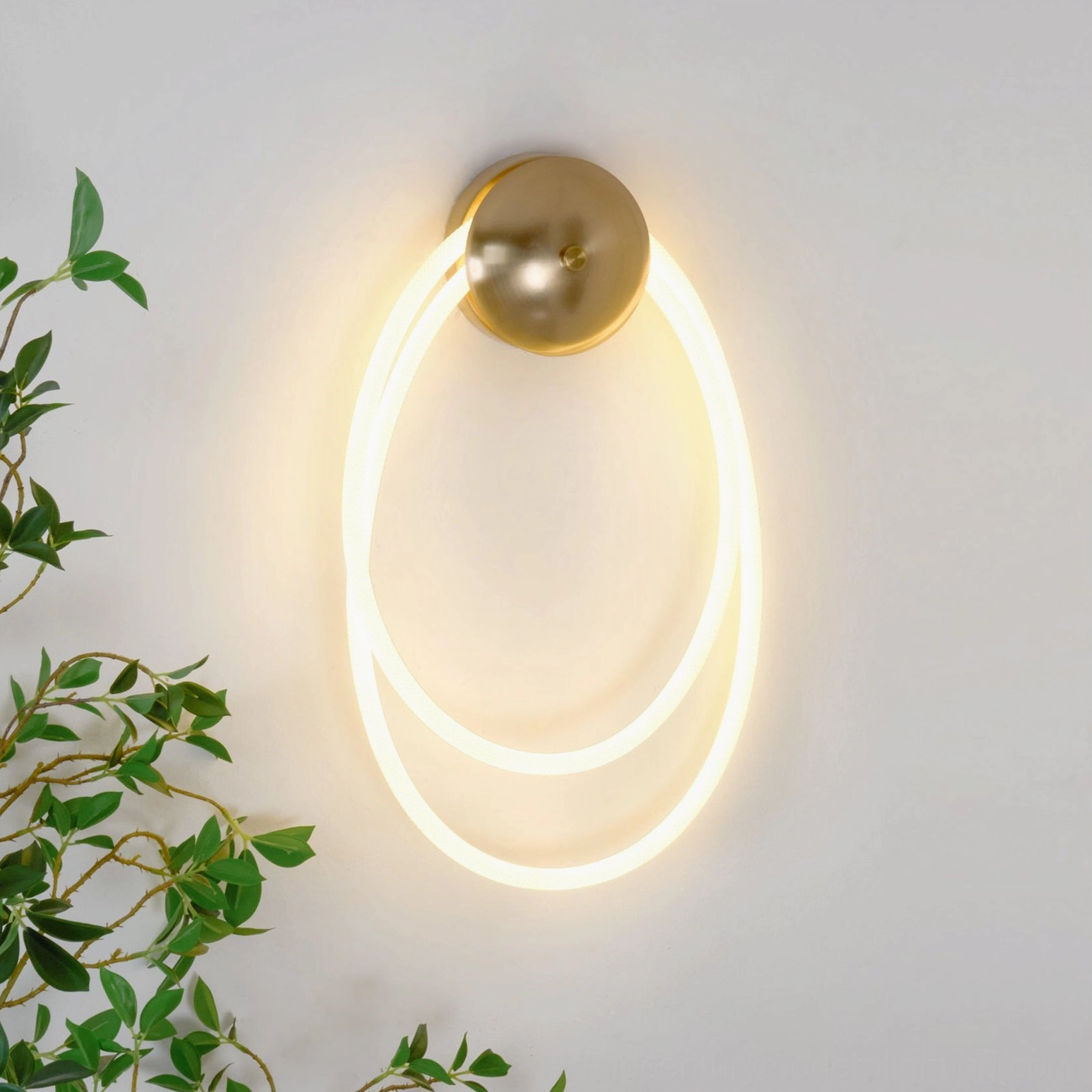 Rigel modern wall sconce with warm LED glow mounted on interior wall with green plant decor