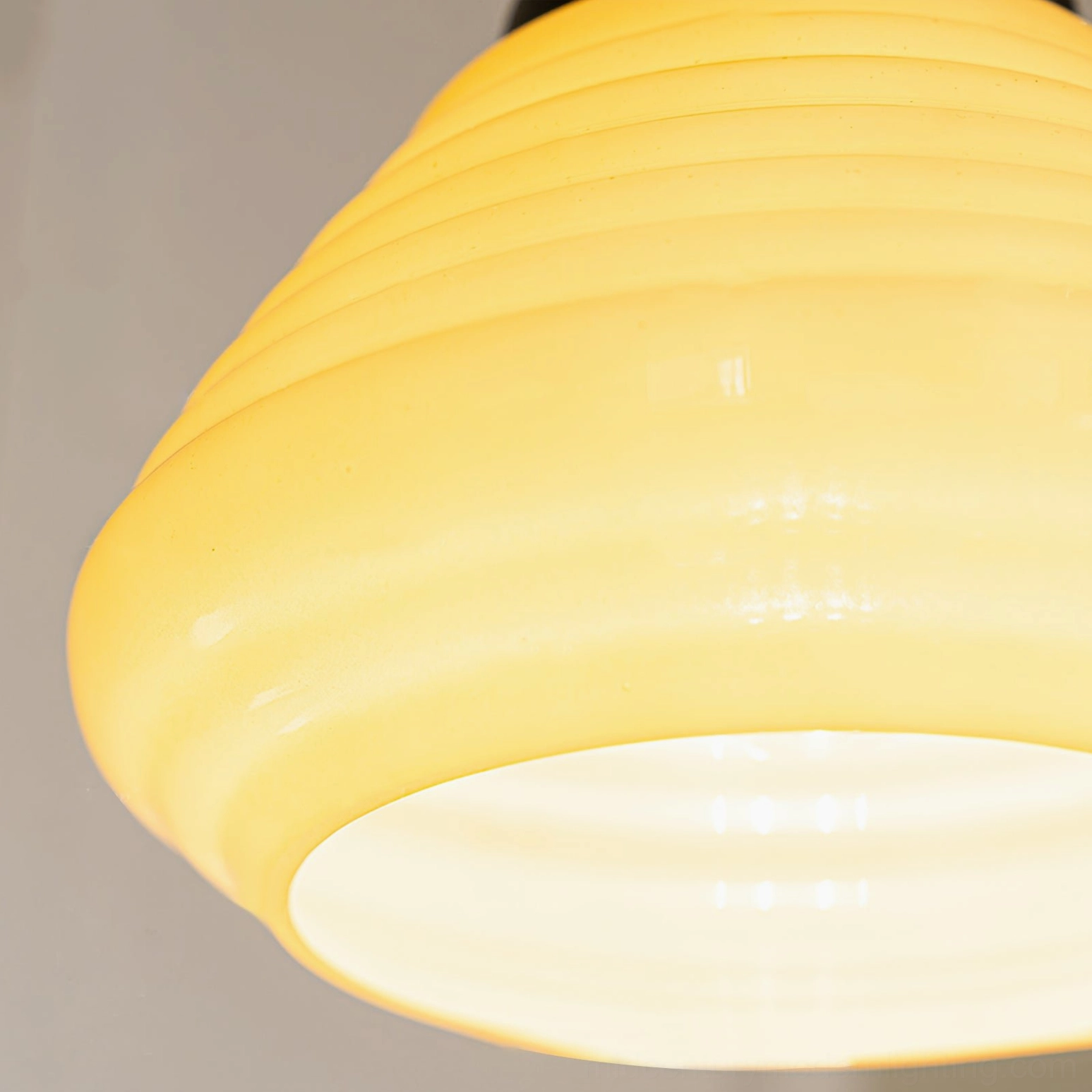 Illuminated rippled glass shade of wooden pendant light showing warm yellow glow and horizontal ribbed texture detail