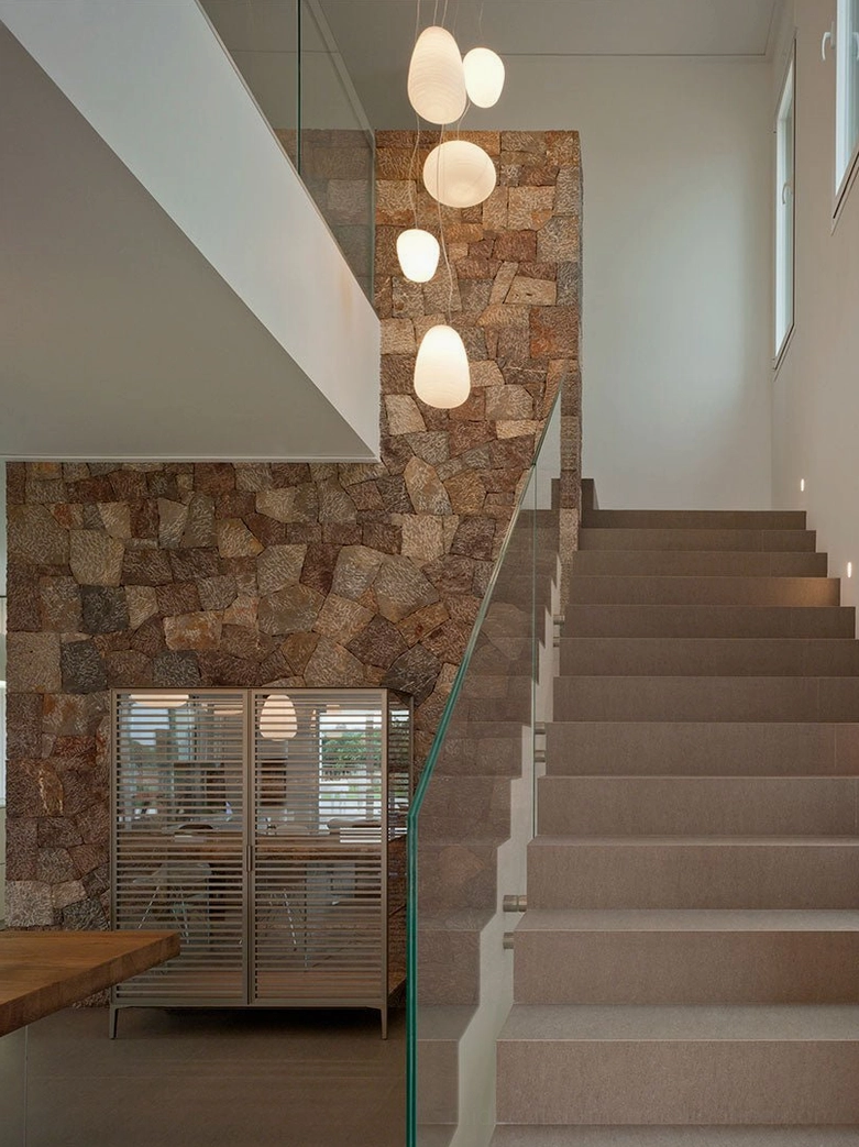 Rituals pendant lights linear arrangement stairwell modern residential stone wall interior