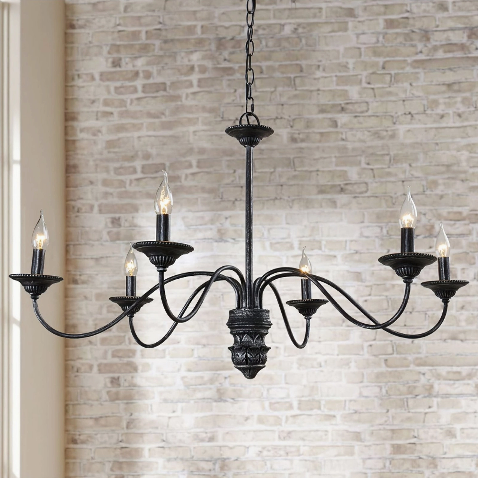 Rohan 8-light black farmhouse chandelier close-up frontal view showing light-colored brick background and ornamental details