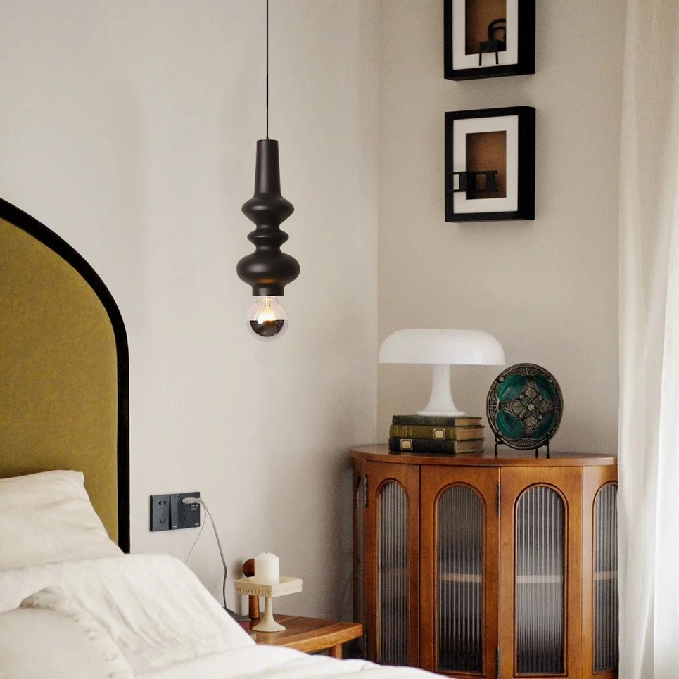 Rudd stacked cylindrical pendant light in matte black with exposed decorative bulb in warm bedroom setting