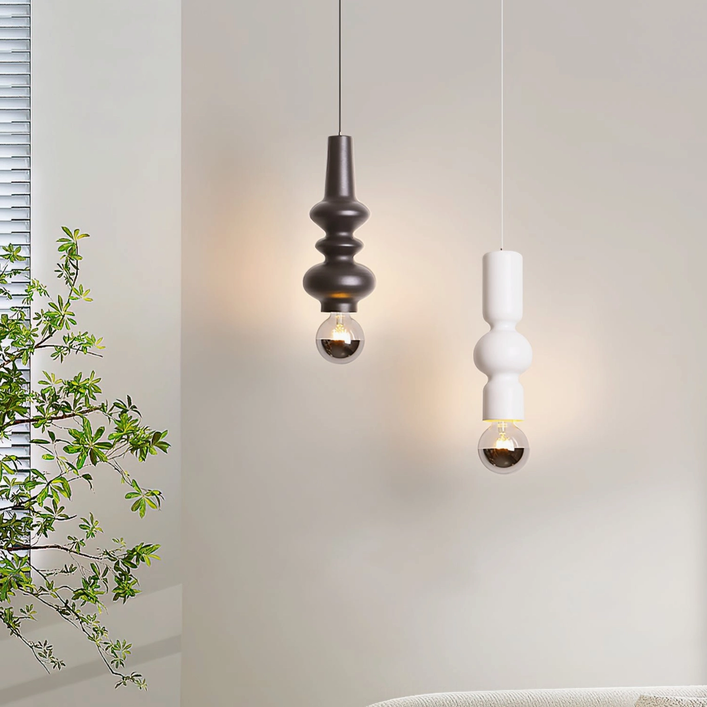 Two Rudd pendant lights in black and white cylindrical design hanging in modern bedroom with potted plant