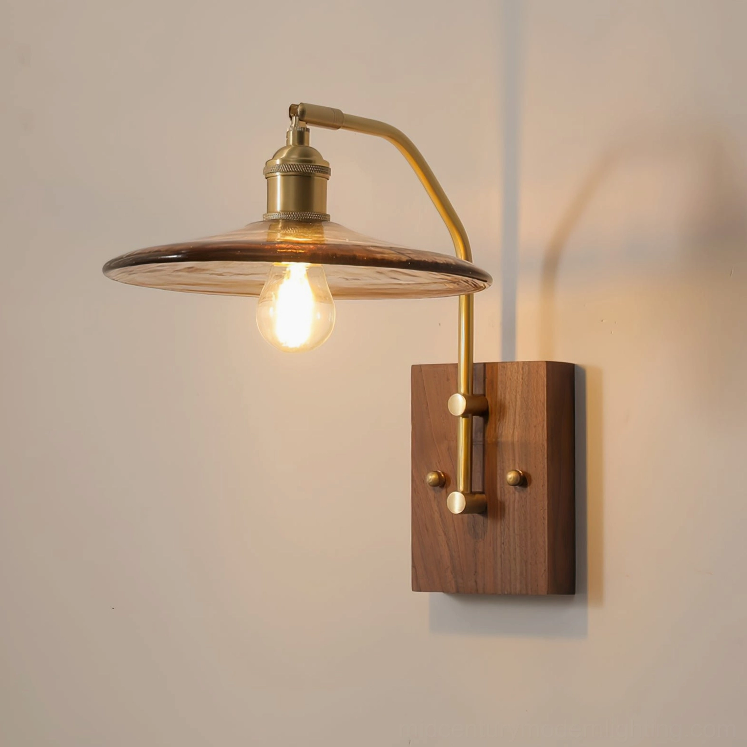 Close-up detail of Runia wall lamp showing curved brass arm and exposed Edison bulb filament against warm neutral wall