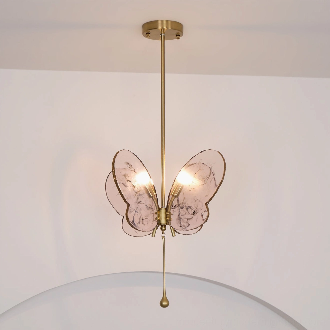 Overhead photograph of pink butterfly pendant lamp in modern room with brass suspension and curved decor