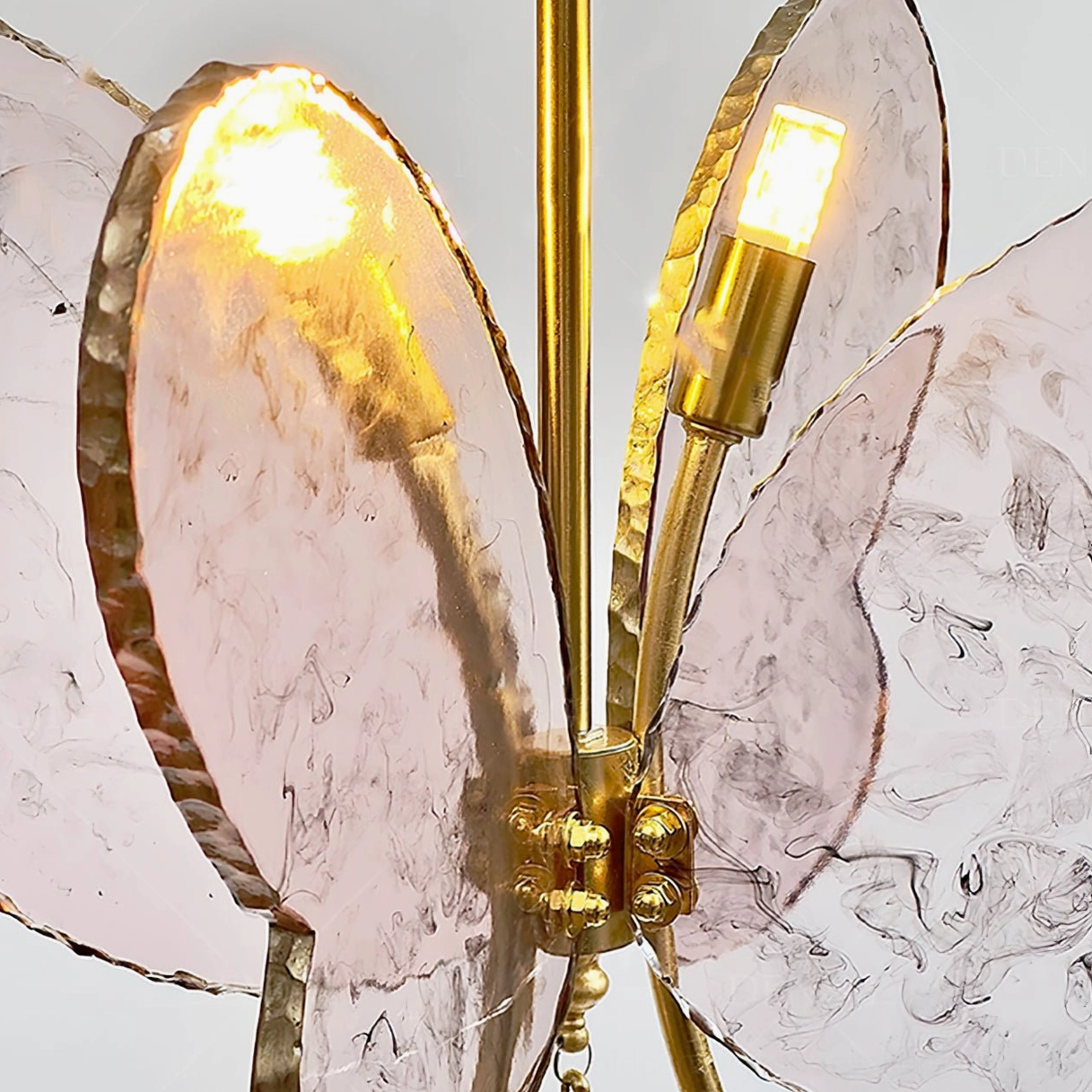 Illuminated pink butterfly pendant lamp with warm glowing bulbs and visible brass hardware joints