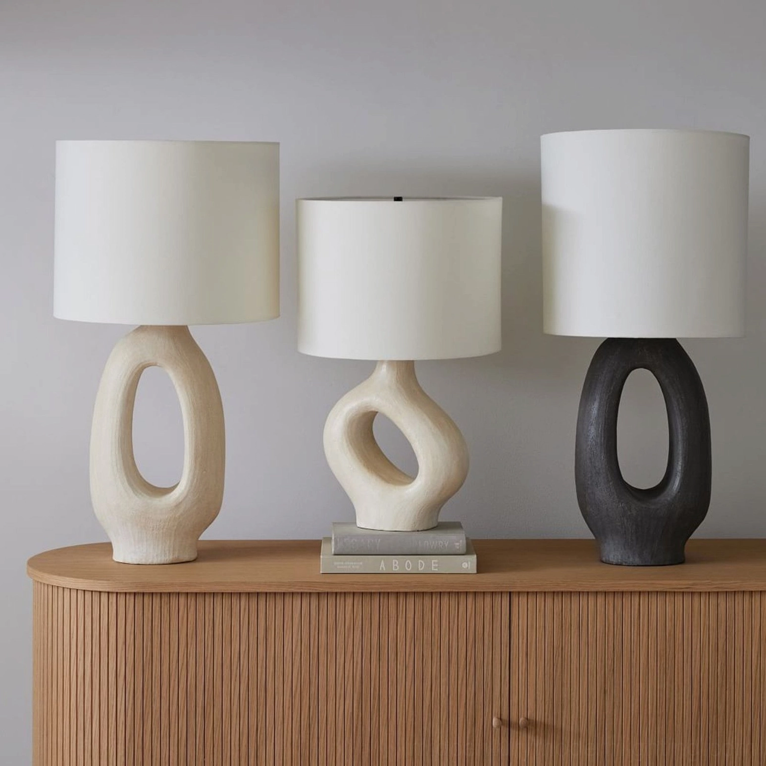 Set of three Sauce sculptural table lamps with mixed finishes displayed on wooden fluted sideboard with white fabric shades