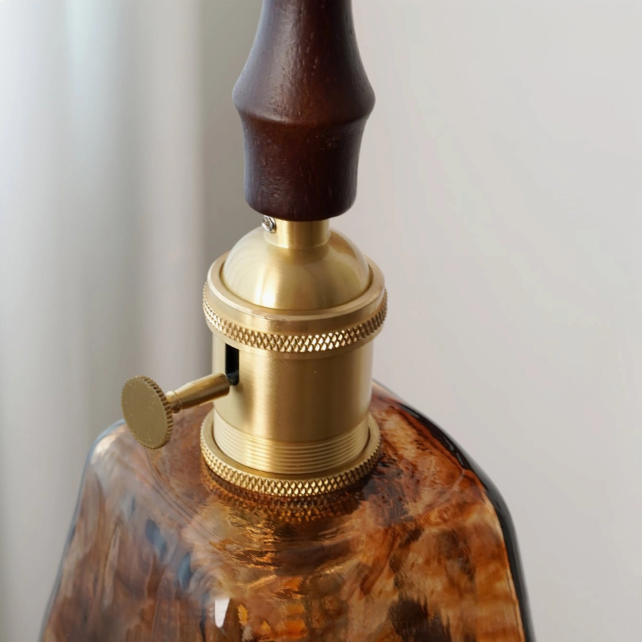 Sculptural amber pendant lamp showing walnut wood handle and glass curves in minimalist home setting