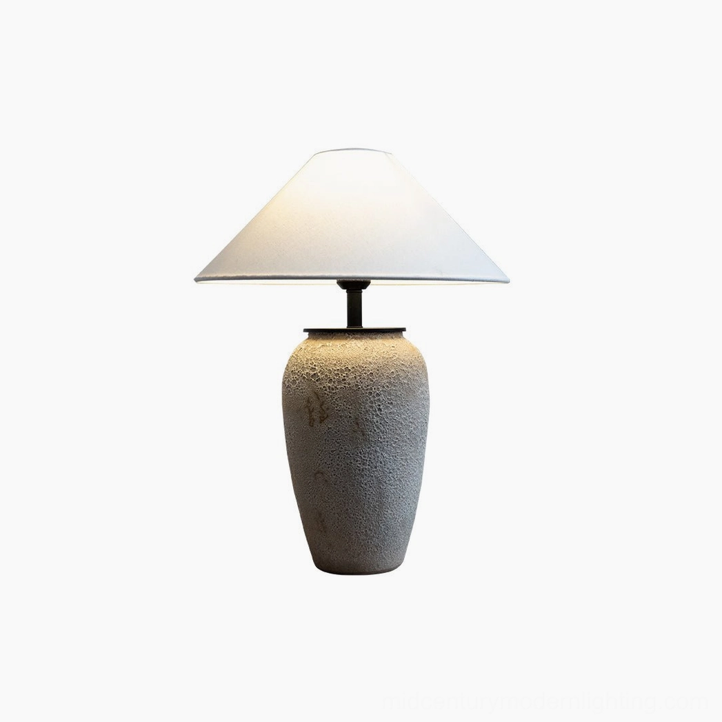 Sculptural ceramic table lamp with textured stone-like base and conical cream fabric shade