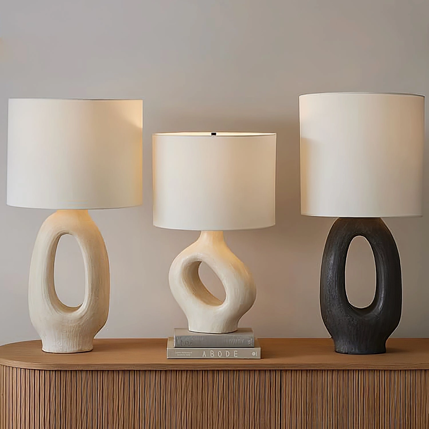 Three handcrafted resin base table lamps styled with decorative book accents on minimalist wooden sideboard