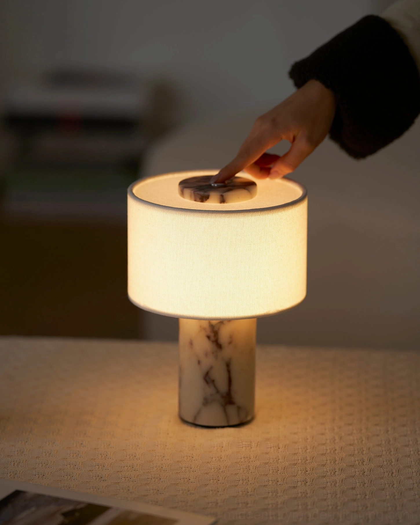 Finger touching white fabric drum shade crown switch of Sediment marble table lamp