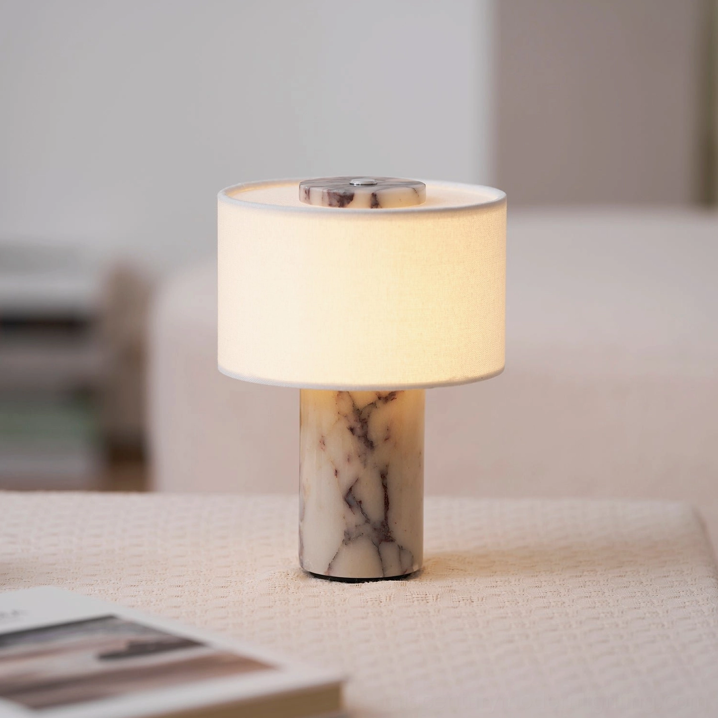 White marble cordless lamp creating soft glow on fabric sofa side table, minimalist interior design