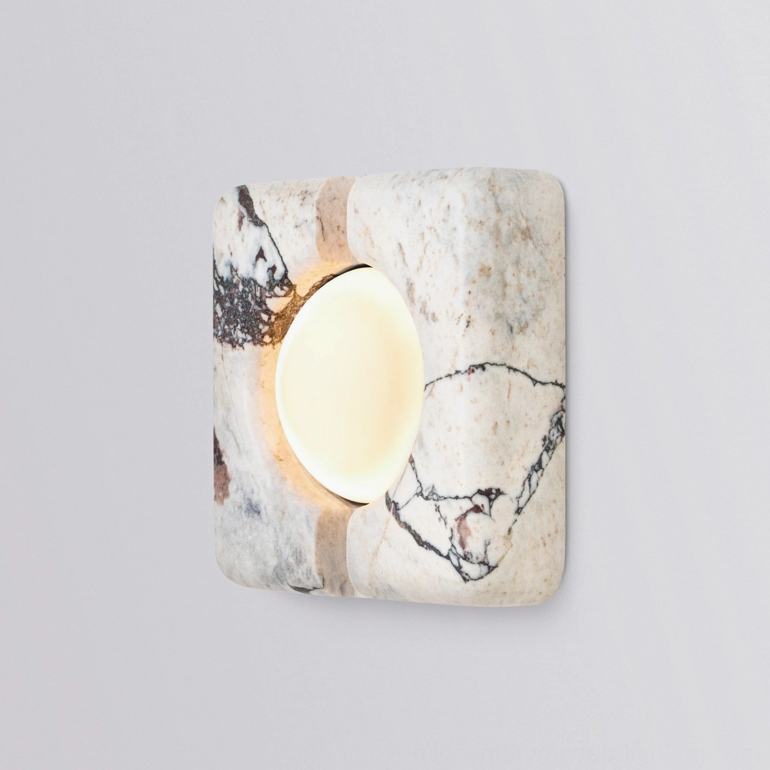 Three-quarter view of illuminated stone wall lamp with warm LED light and natural veining