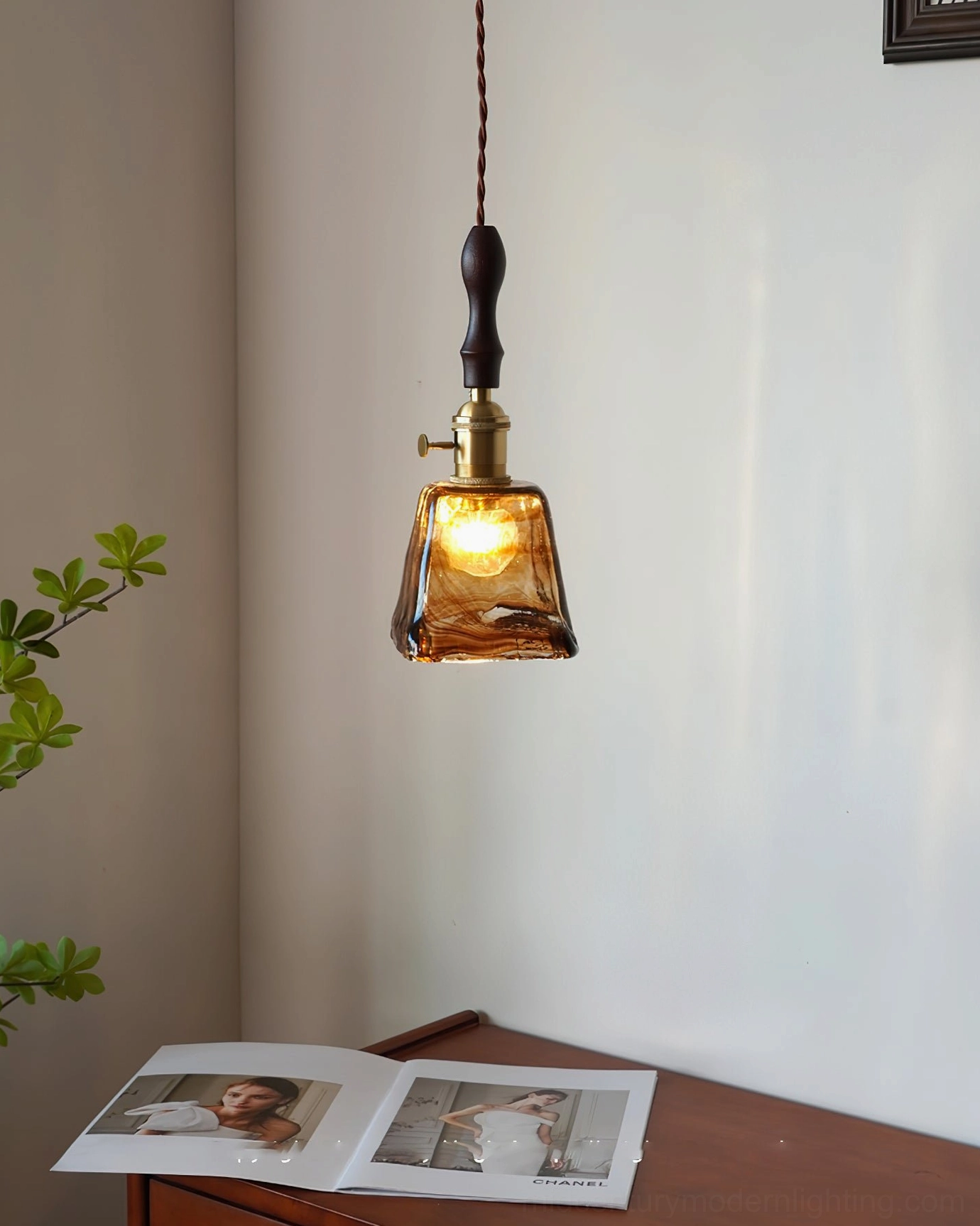 Small wavy glass pendant lamp in minimalist workspace with potted plant and wooden desk, modern lighting