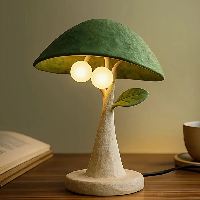 Front-facing view of Soloma resin table lamp with sage green matte canopy and frosted glass diffusers, sitting on wooden bedside table with book and coffee