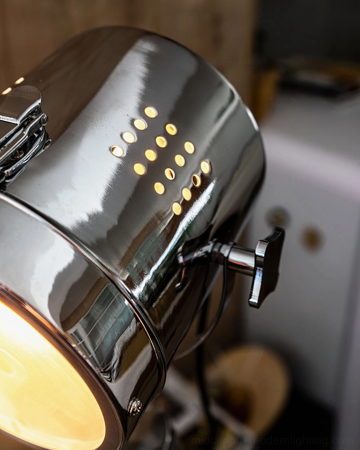 Close-up side view of illuminated spotlight lamp head with heat dissipation holes and metal adjustment knob, warm LED bulb detail