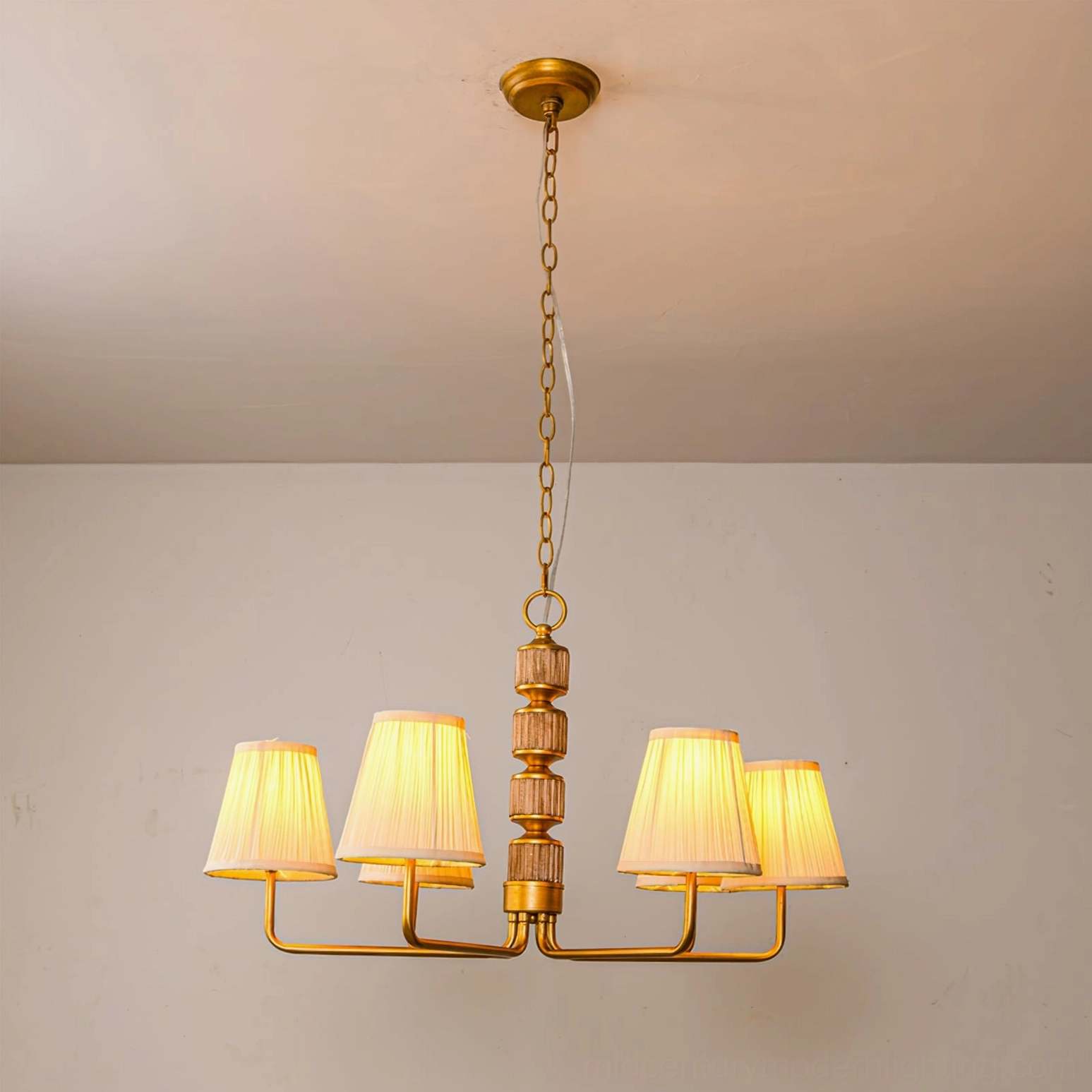 4-arm brass gold Stacey chandelier front overhead view with warm glowing light illuminating pleated fabric shades and golden hardware