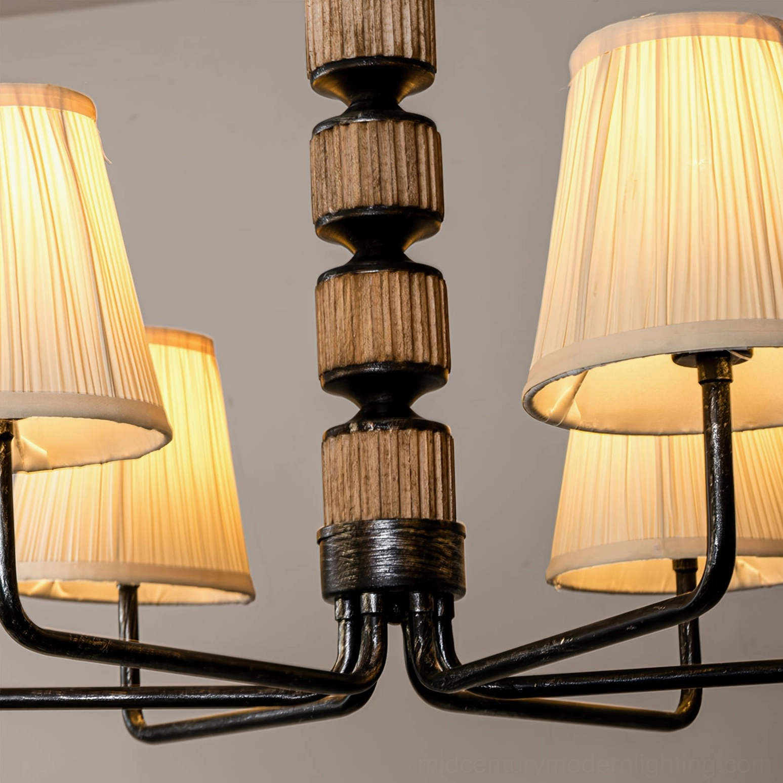 Front overhead close-up of illuminated Stacey chandelier showing black metal arms, stacked wood-metal central pole and glowing shades