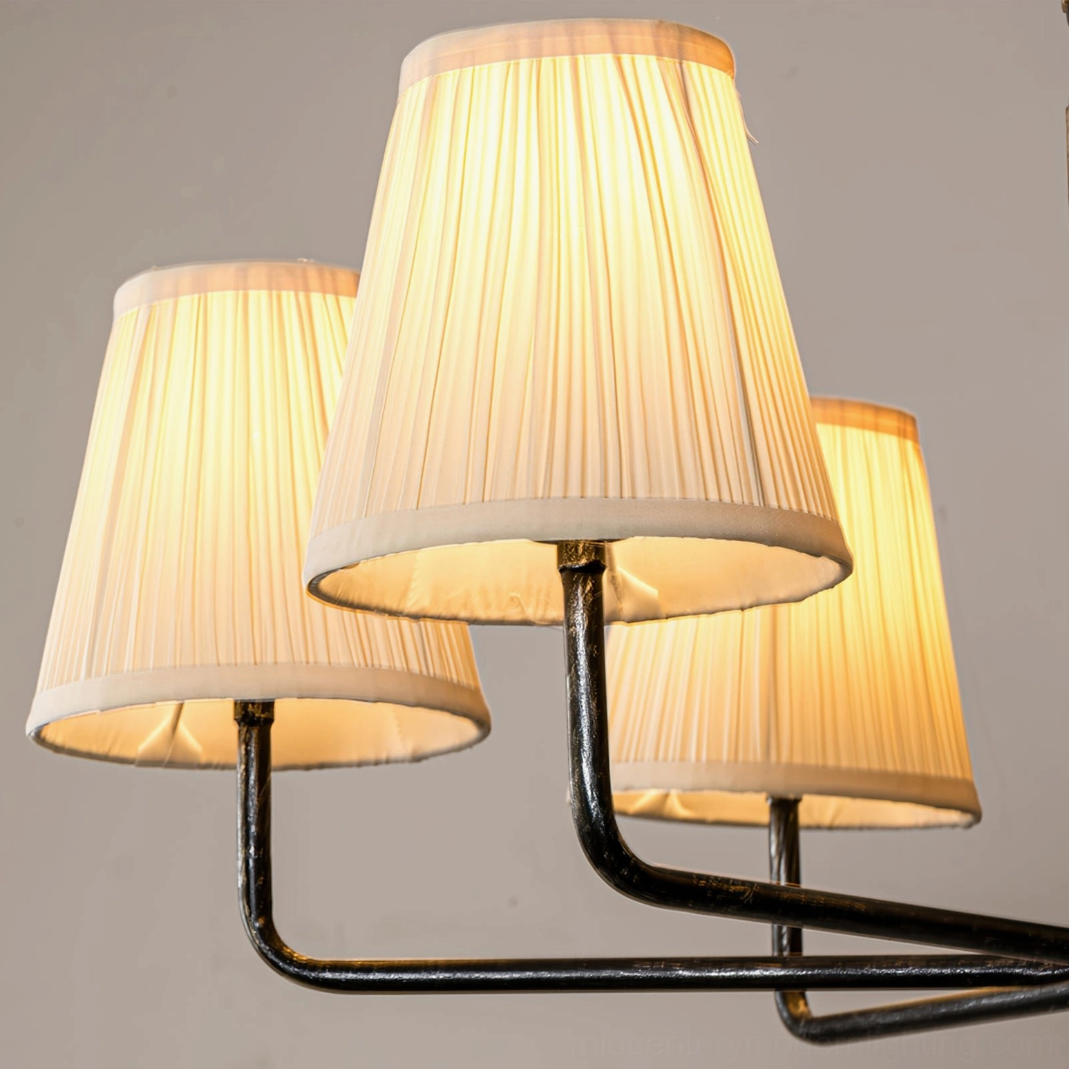 Lit Stacey 6-arm chandelier low-angle front close-up showing warm glowing light through pleated off-white fabric shades