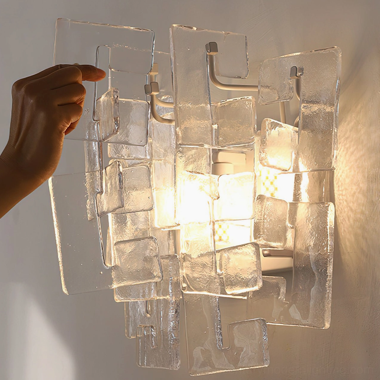Stagger cast glass sconce clear variant illuminated with hand scale reference warm studio light