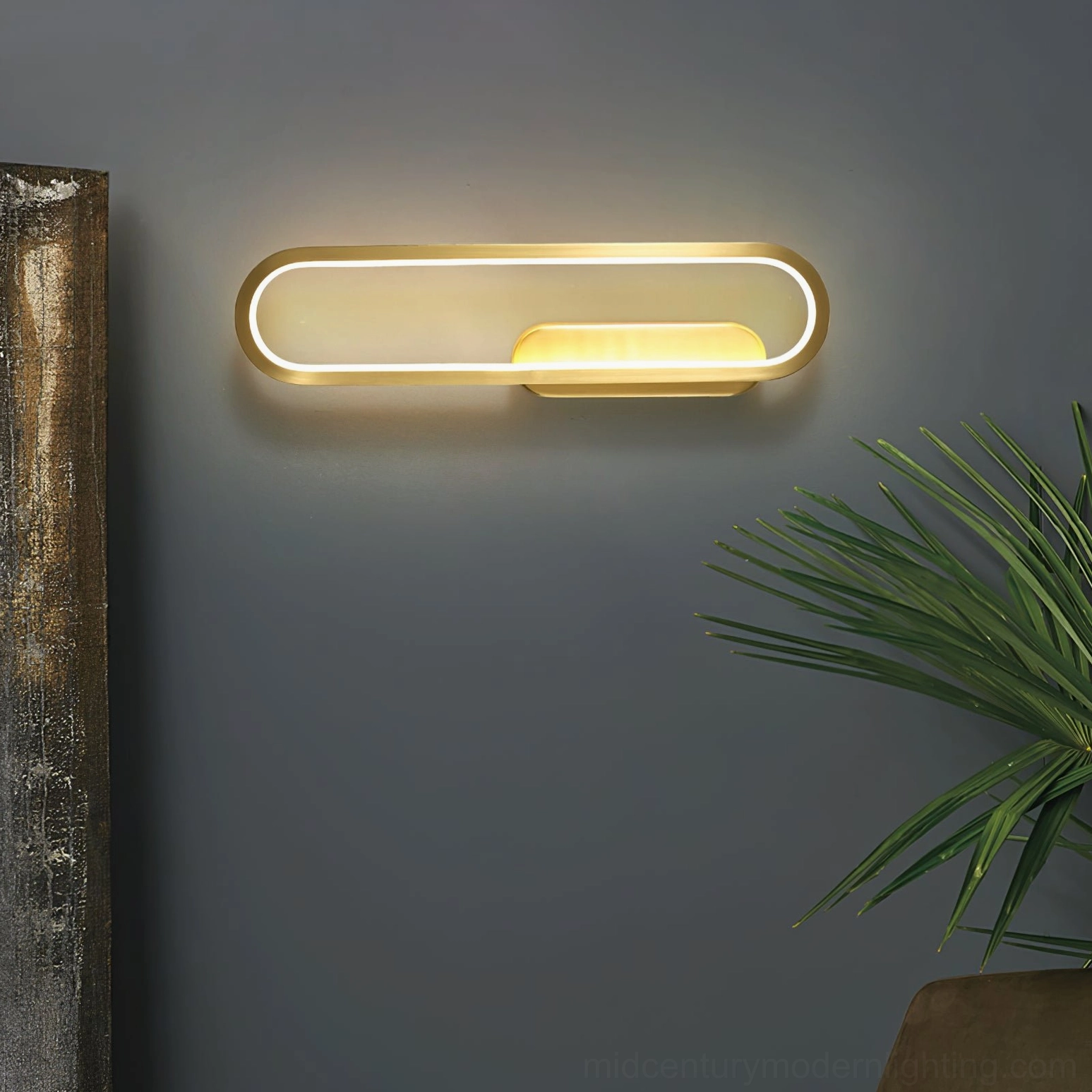 Horizontal gold brass LED wall sconce in modern living room with gray walls and green plant décor