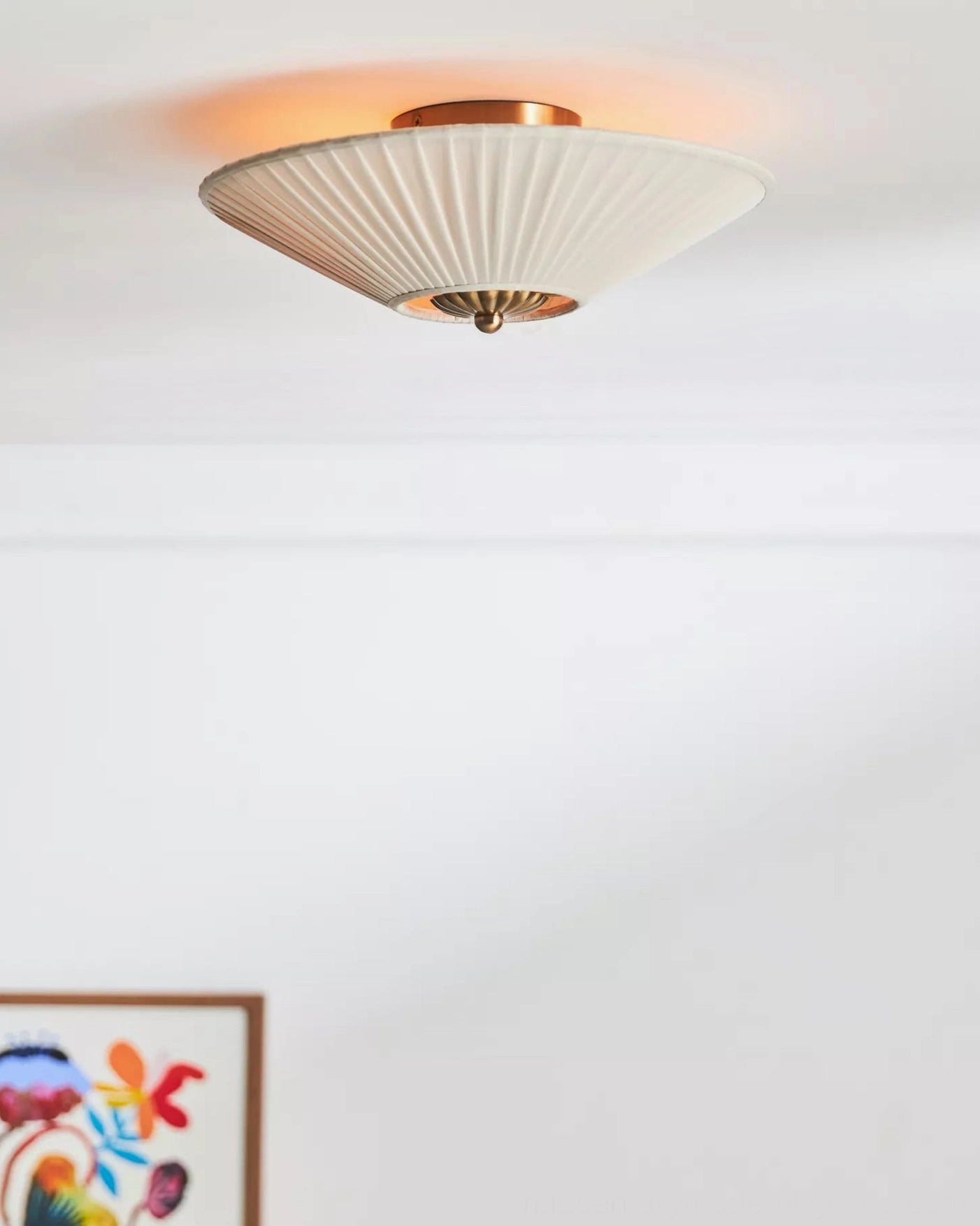 Stefanie small conical pleated ceiling lamp with warm ambient light in modern home with colorful framed artwork on wall