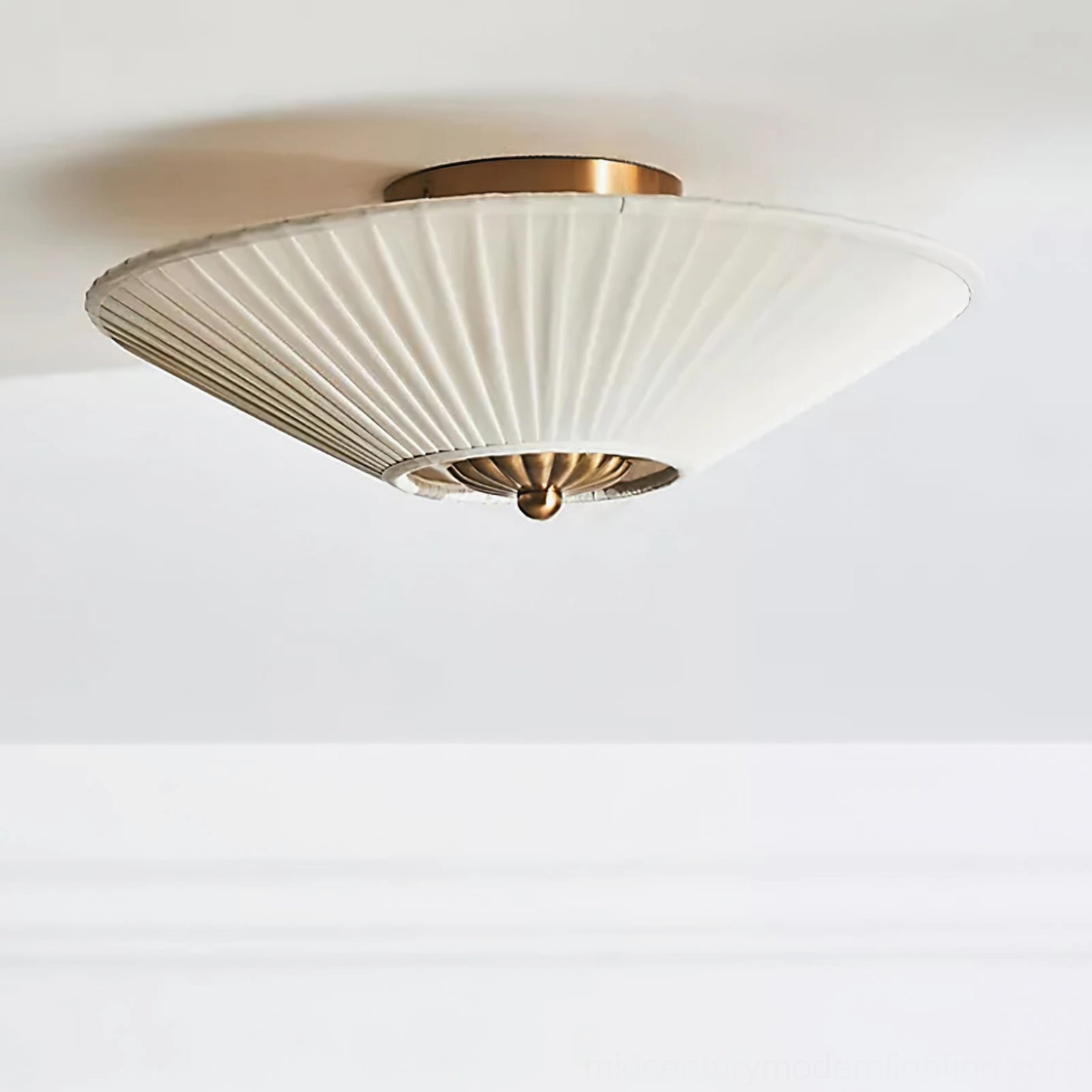 Stefanie semi-flush mount lamp side view featuring wide off-white pleated shade and polished brass mounting cap against white wall with crown molding